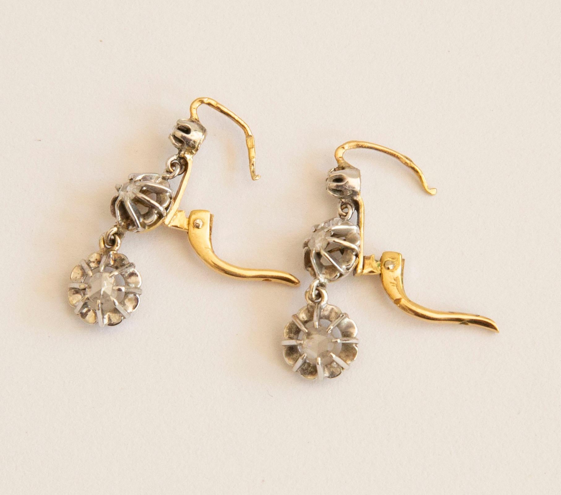 An antique pair of Victorian 14 karat yellow gold drop earrings, each set with 3 rose cut diamonds in a silver mirror chaton. The earrings feature a hinged hook closure. The earrings were made during the late Victorian period in the late 19th