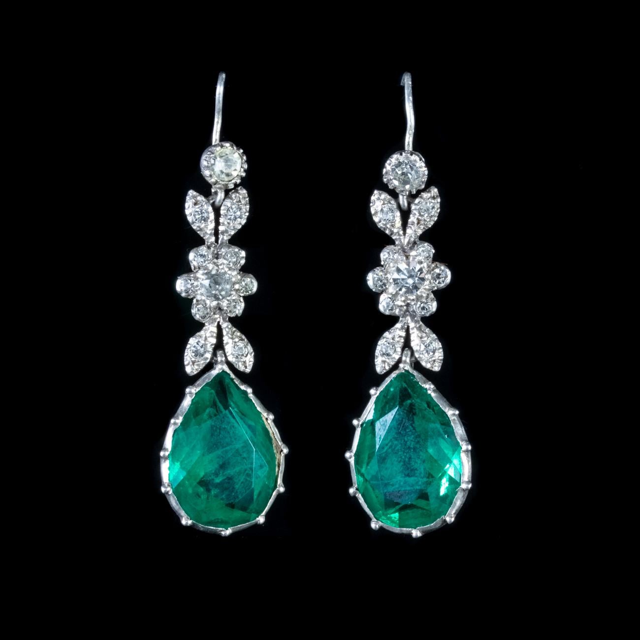 These gorgeous Antique Victorian earrings are modelled in Silver to form beautiful floral shapes. Each earring is set with an array of white Paste stones into the floral sections and below sits a large green Paste dropper, which shines like a