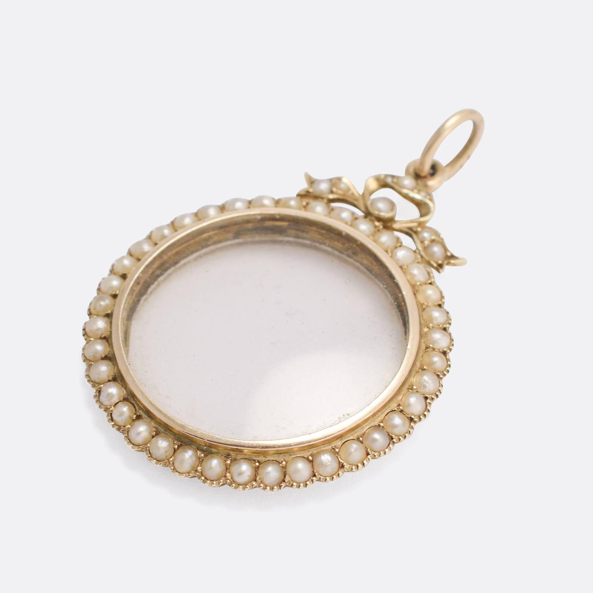 An elegant antique round locket, set with pearls and finished with a bow on top. It's modelled in 9k gold throughout, with a glass front and back locket compartment. The locket is easily accessible from the reverse, allowing for a photograph or
