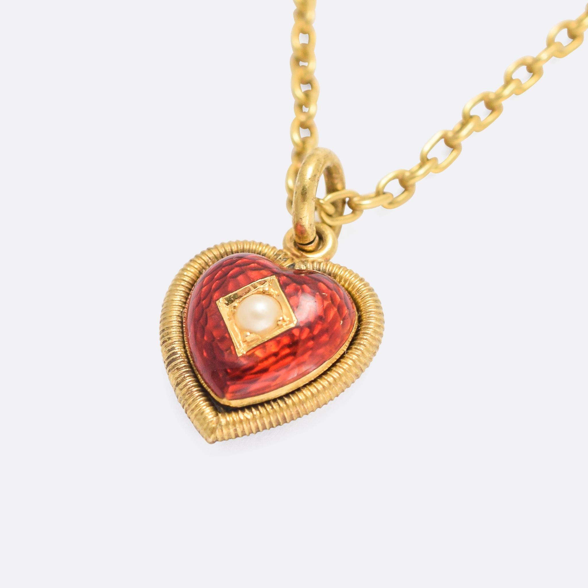 A sweet antique heart locket set with a single pearl and finished in red guilloché enamel. It dates from the late 19th Century, circa 1890, with a ribbed gold surround. The pendant is modelled in 15 karat gold, and offered with a period 18k