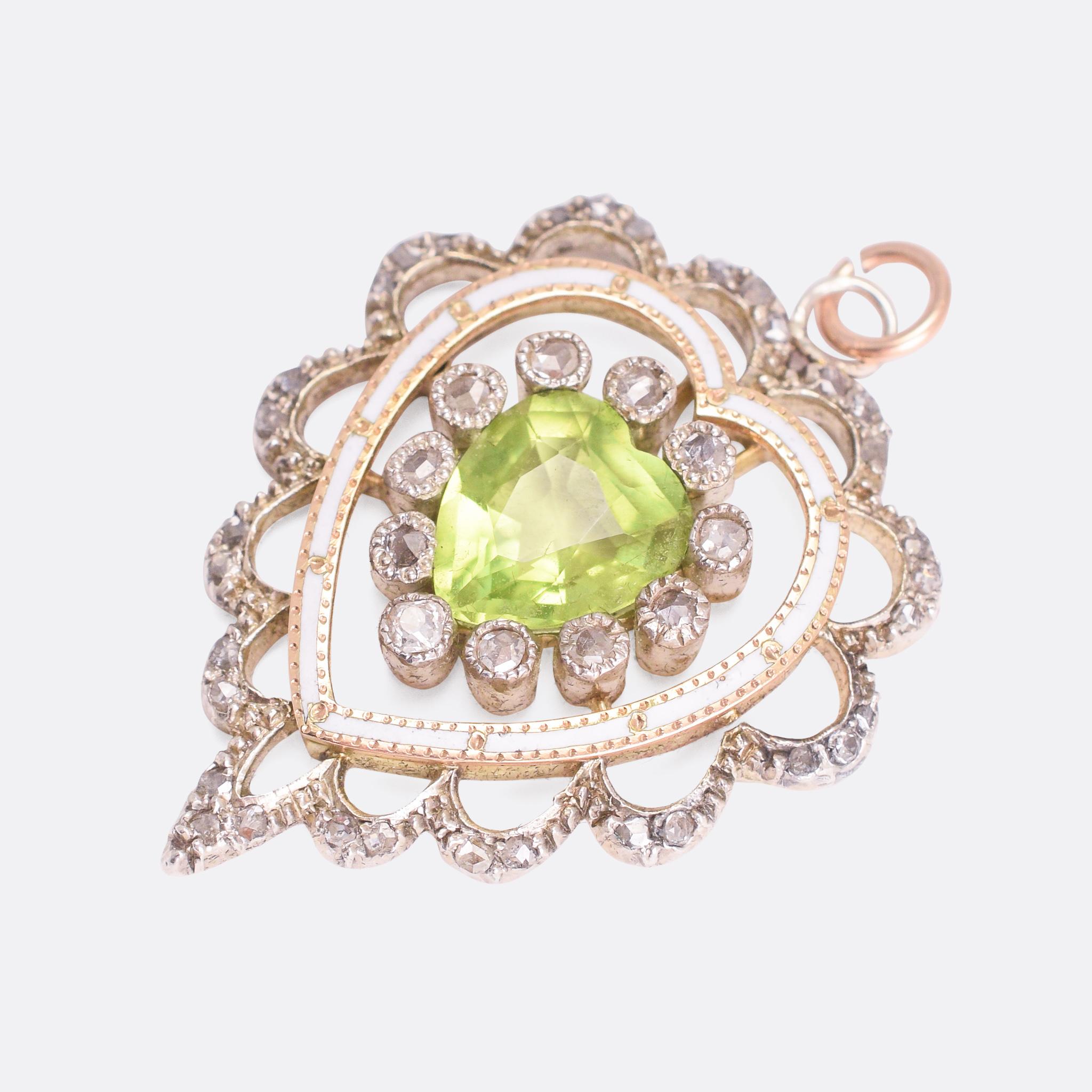 A beautiful antique heart pendant featuring intricate openwork and fine white enamel. The central stone is a vivid green peridot, embellished by rose cut diamonds within a heart motif. It dates from the latter part of the 19th Century, crafted by
