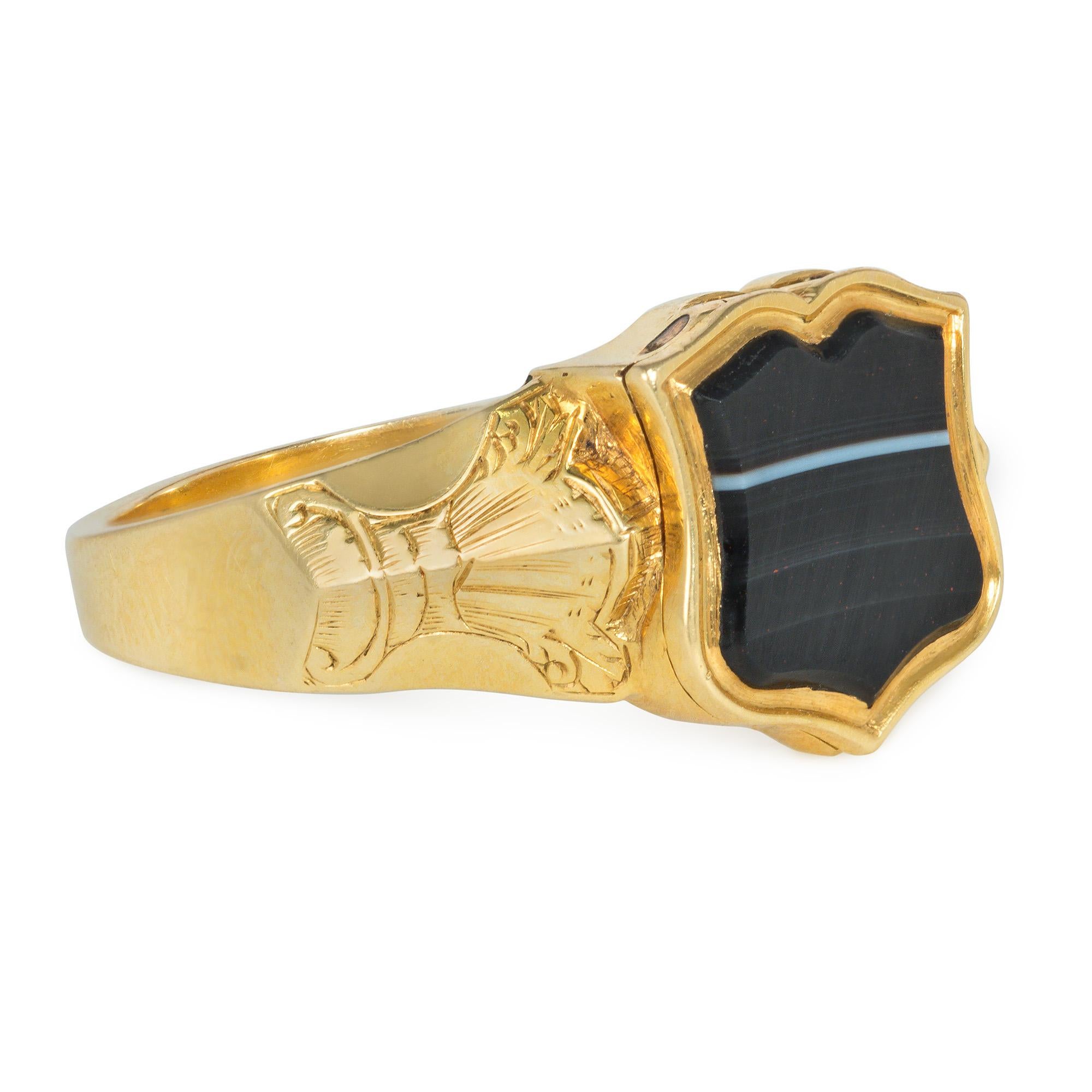 A Victorian gold poison ring set with a shield-shaped sardonyx plaque which opens to reveal a hidden compartment and interior locket in an engraved foliate mounting, in 18k. Inscribed and dated January 8, 1844

Center plaque measures approximately