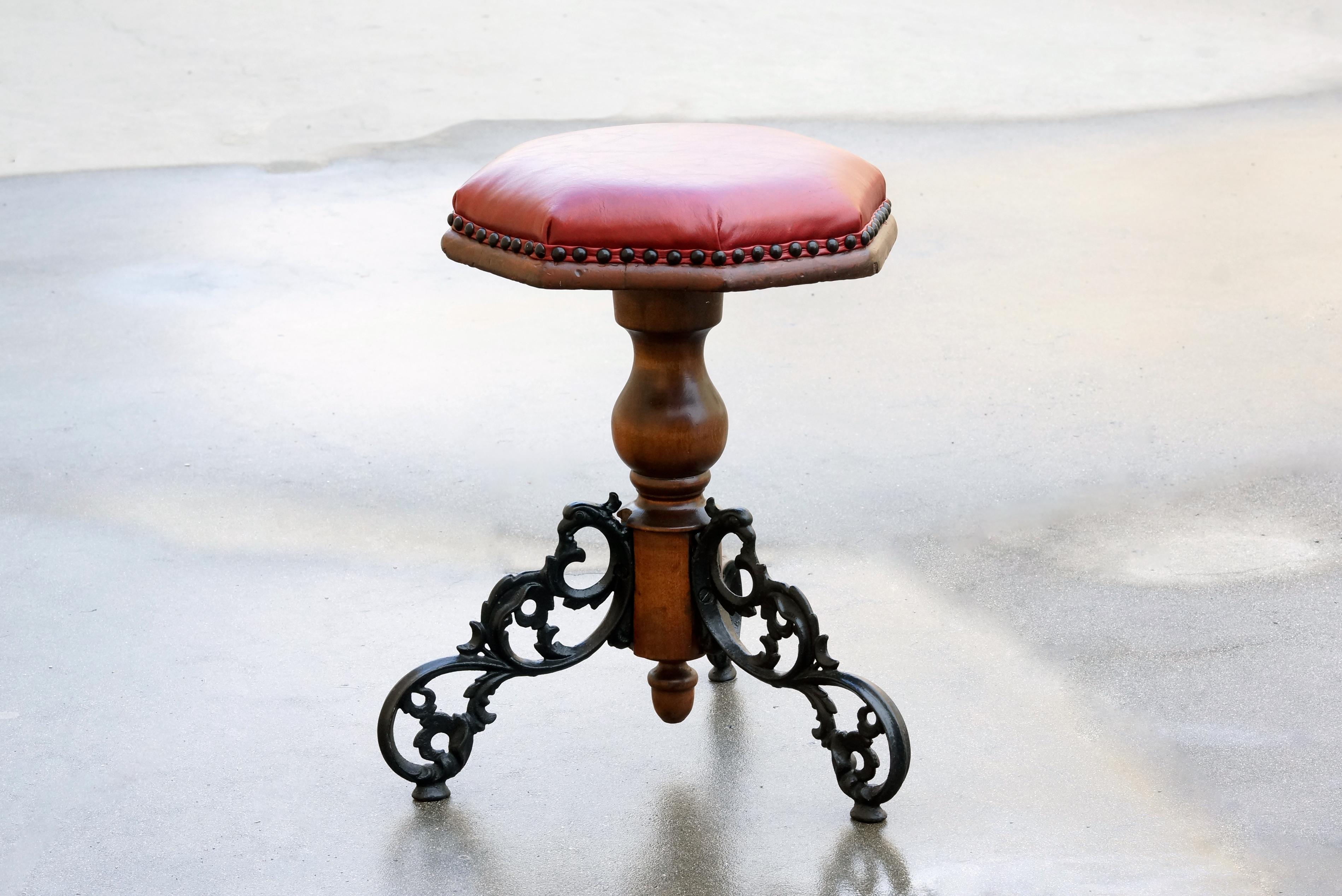 This 1920s oak piano stool features lovely cast iron legs and new red leather with black upholstery tacks. This refinished antique is in very good condition for age and use; please note slight warp to seat as pictured. 

Dimensions: 17