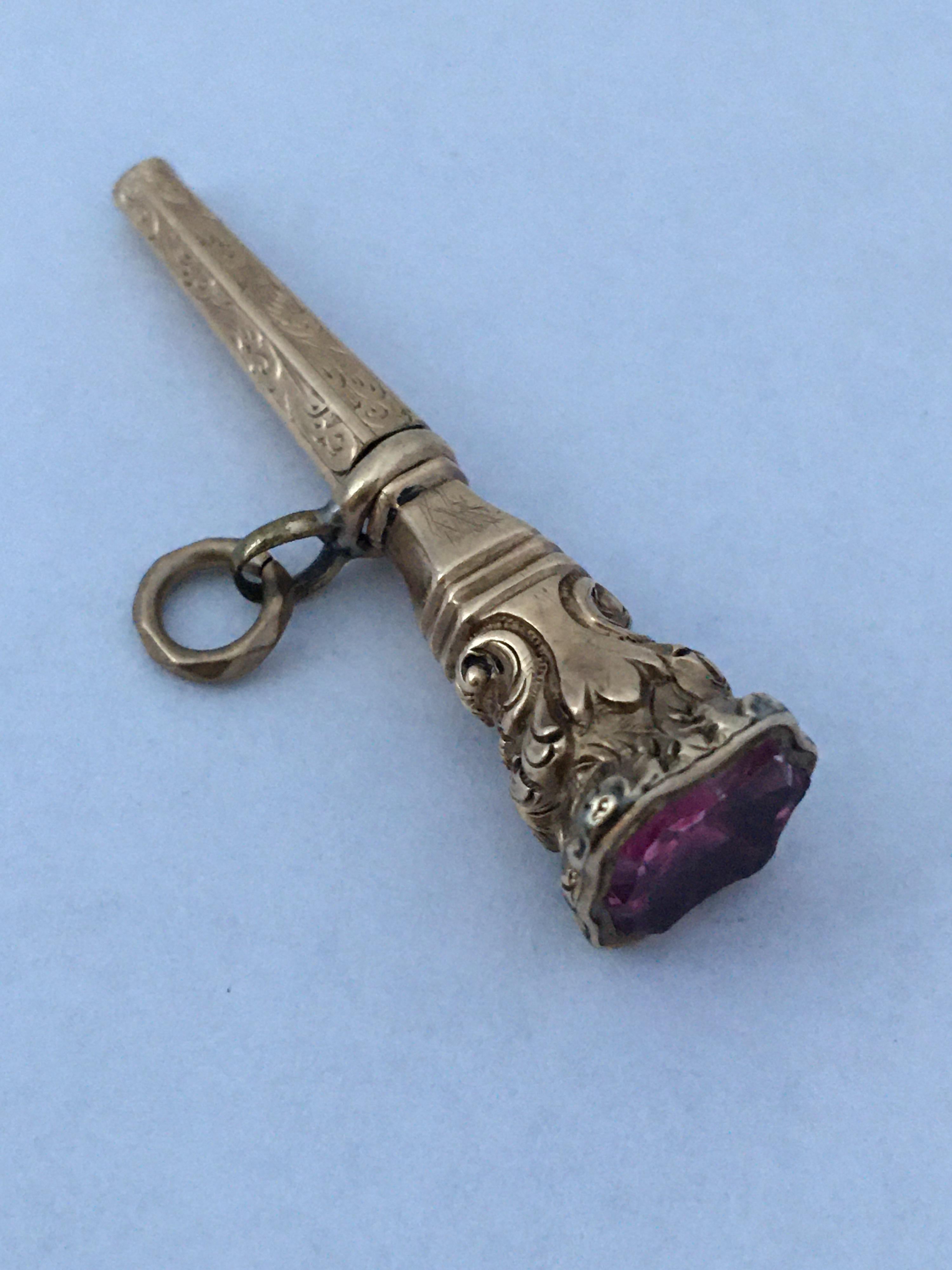 This ornate Gold Antique Victorian Watch Key Pendant features a dark pink Paste on the base and wonderful detailing throughout, modelled in finely engraved and carefully carved Gold cased metal.

Originally used to wind up a pocket watch, this would