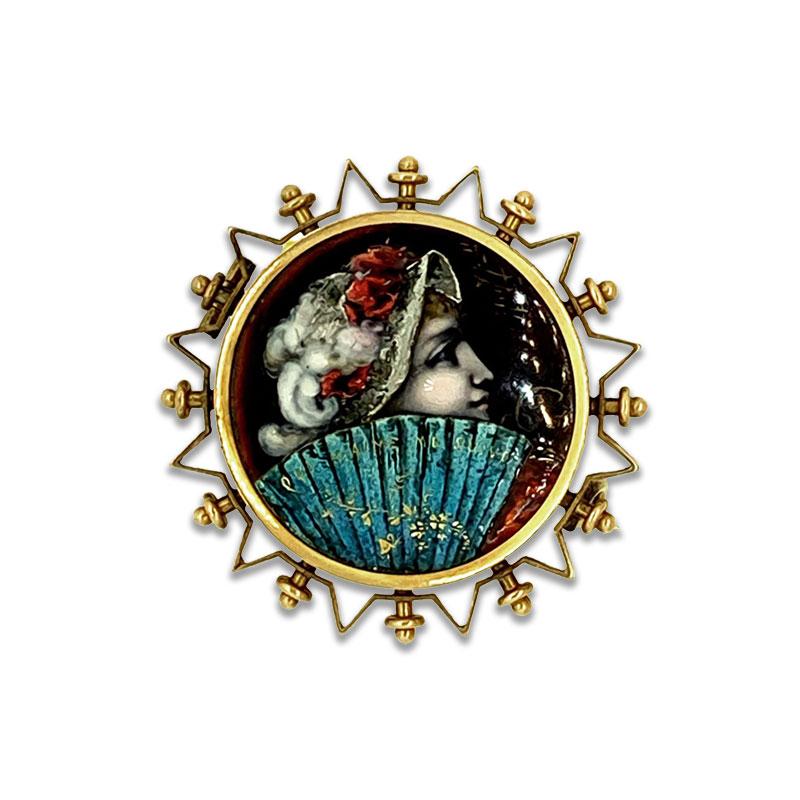 A lovely Victorian brooch with perfect artwork depicts a young woman behind a blue fan with a charming message, “Qui m’aime me suive,” meaning “Whoever loves me follow me.” The vibrant picture is adorned with an 14K yellow gold designed