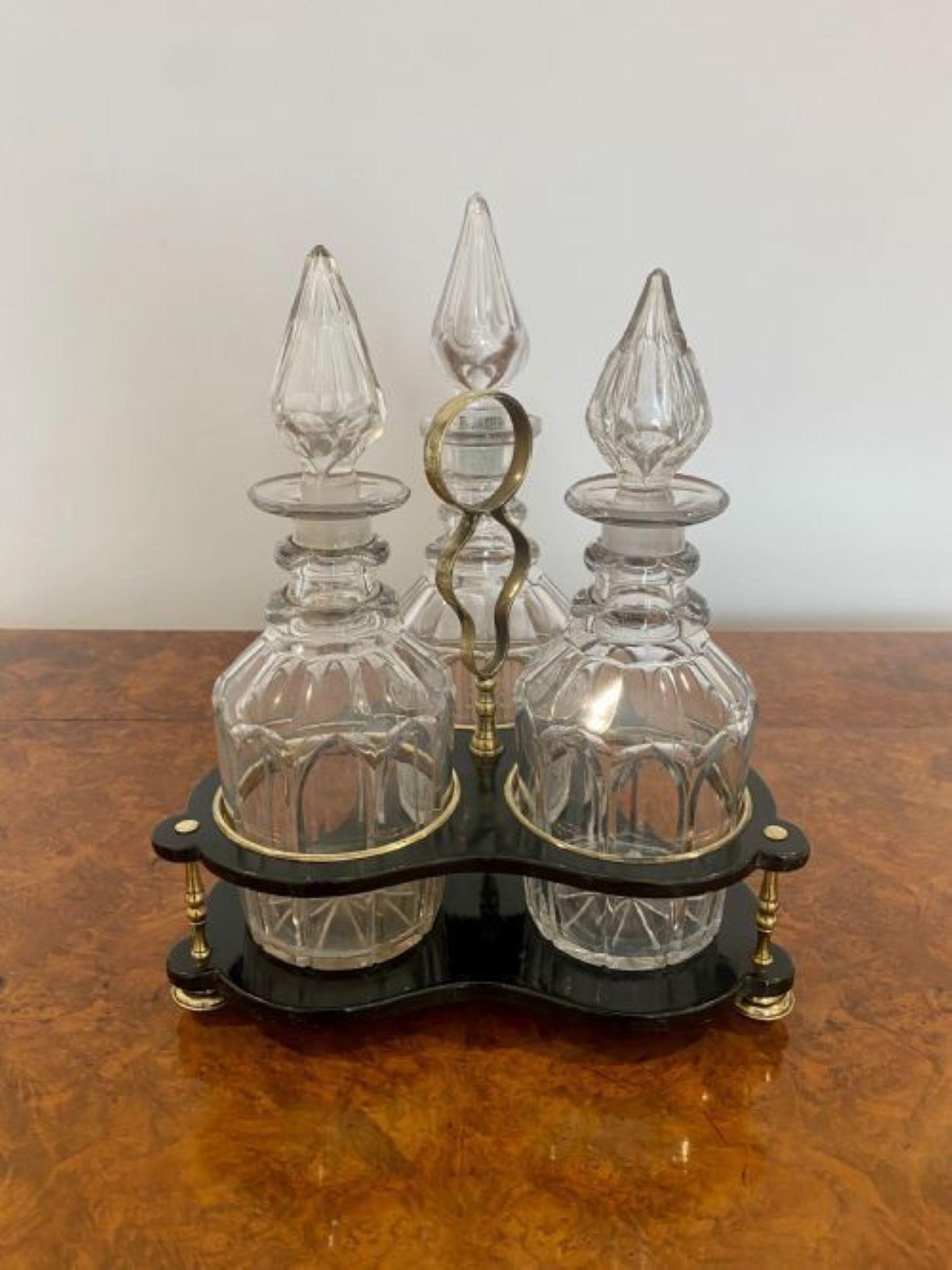 Antique Victorian quality decanter stand with three original cut glass decanters. Quality lacquered decanter stand with three brass columns, feet and a shaped carrying handle, holding the three original cut glass decanters with their original