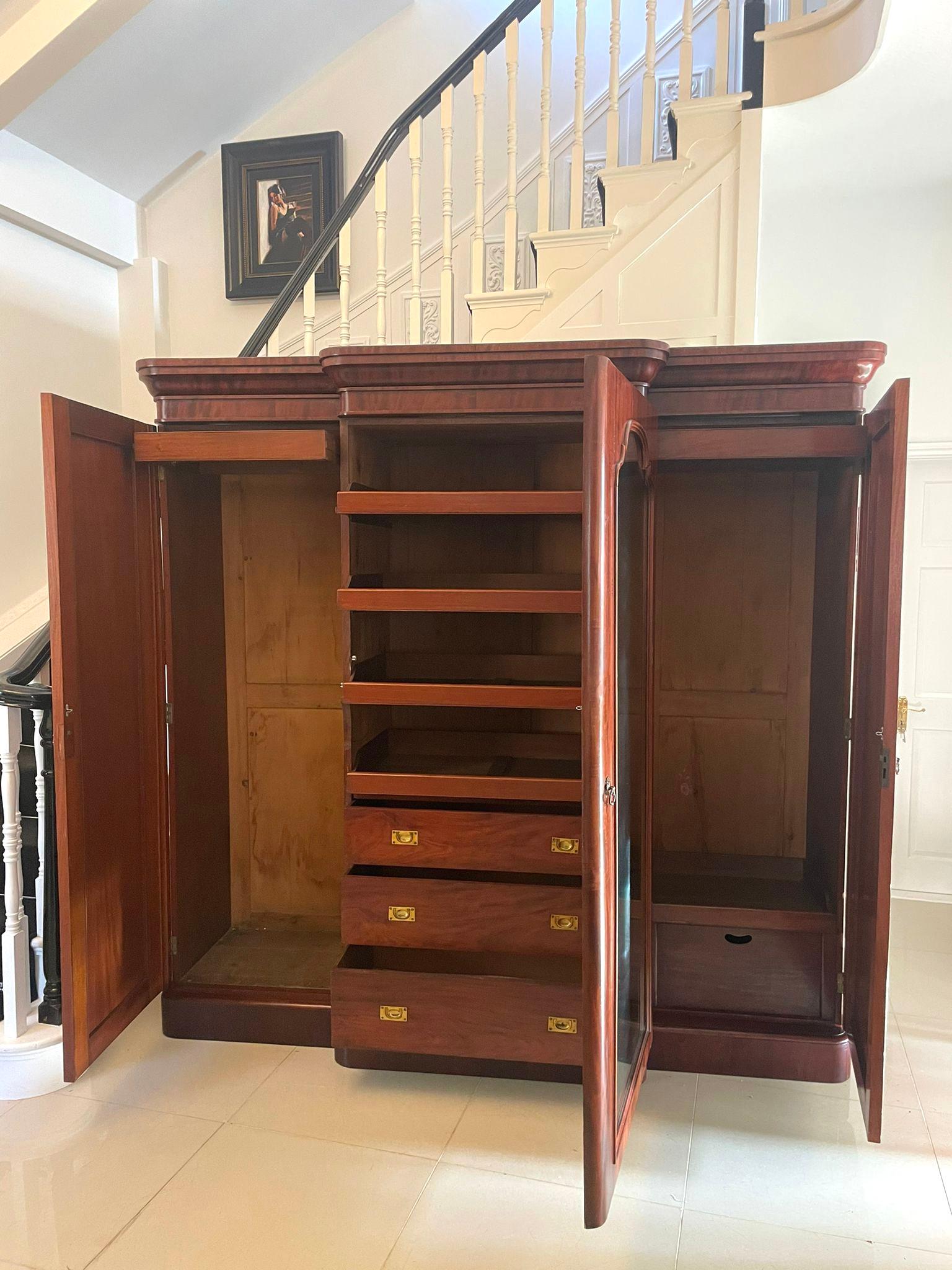 Antique Victorian quality figured mahogany breakfront wardrobe having a quality figured mahogany shaped cornice above a large shaped mirror door opening to reveal a fitted interior consisting of 4 sliding trays and 3 long drawers with original brass