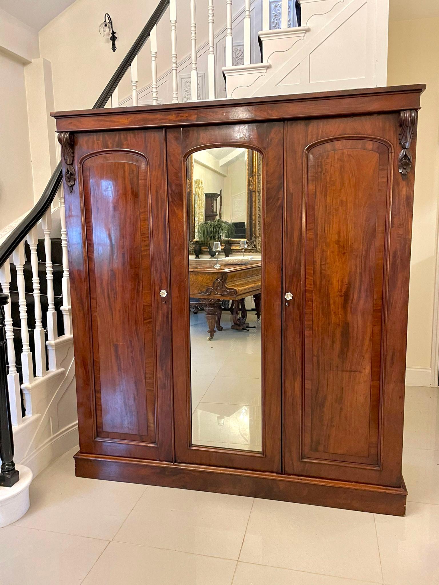 Antique Victorian quality mahogany wardrobe having a mahogany cornice above three doors and attractive quality carvings, mirrored and mahogany door to the centre flanked by a pair of quality crossbanded mahogany moulded doors opening to reveal a