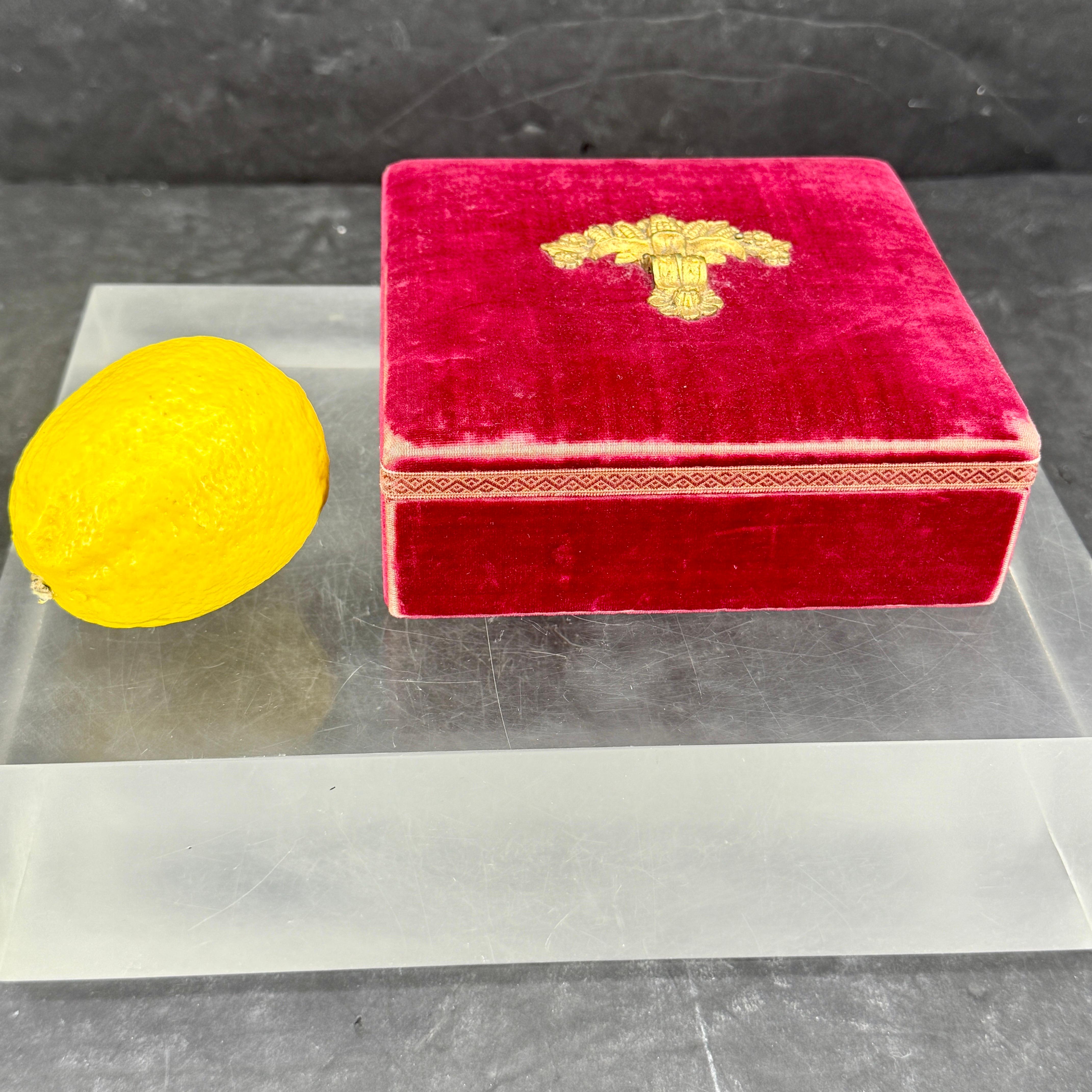 Charmant coffret carré en velours pour bijoux ou bibelots, orné d'une rocaille en métal doré. L'intérieur est doublé en tissu moiré jaune. Merveilleuse pièce pour un meuble de toilette ou une table. 