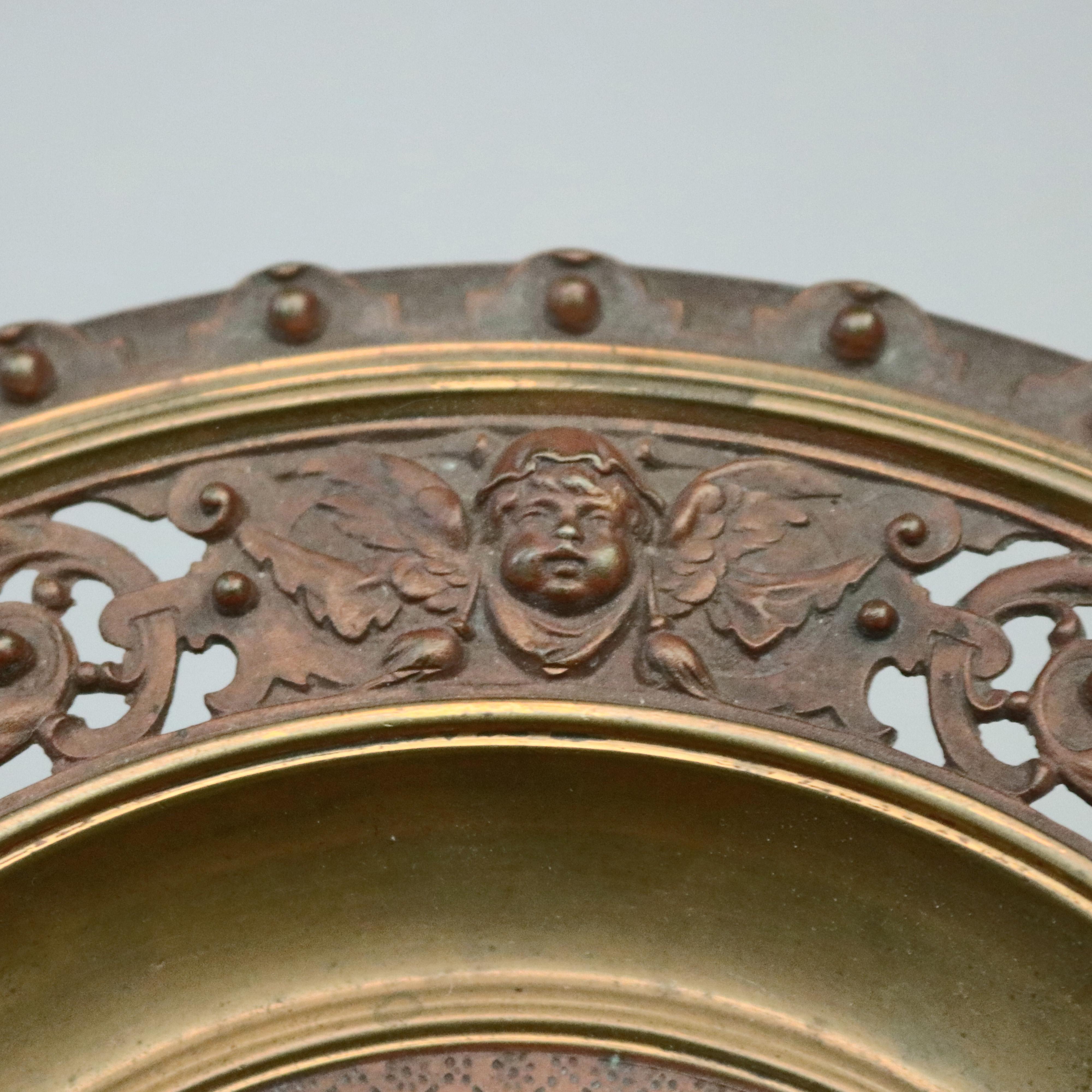 An antique figural card tray offers bowl with central figure and flag with reticulated scroll and foliate rim with cherub masks and having double scroll handles, raised on faceted pedestal with scroll and foliate decorated base, stamped PH