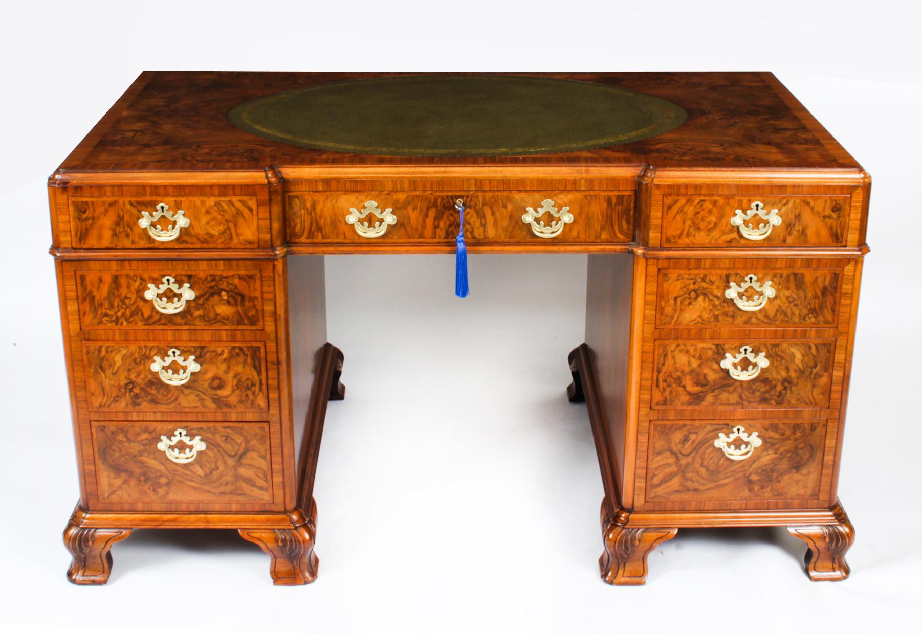 A superb burr figured walnut pedestal desk, dating from the early 20th Century.

Of recessed broken outline, the rectangular top inset with an oval panel of gold tooled green leather, having a wide crossbanded border and a moulded edge with