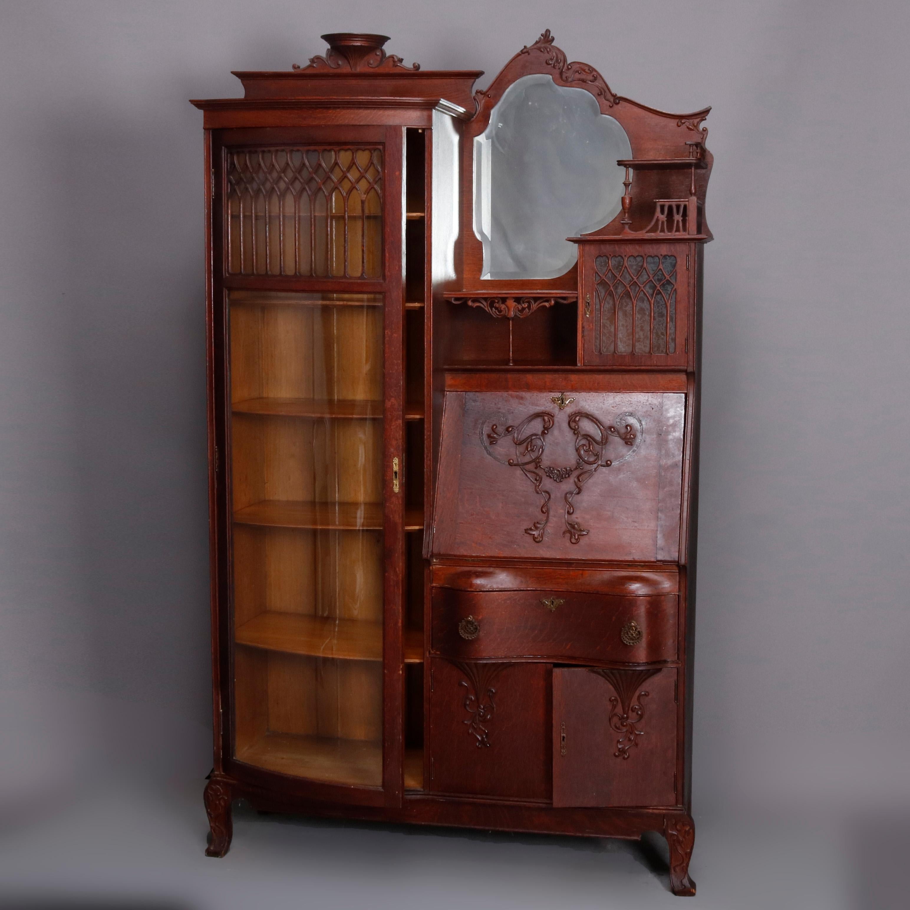 An antique Victorian R.J. Horner style secretary bookcase offers oak construction with urn form crest having flanking foliate and scroll decoration glass front enclosed bookcase, right side with shaped and beveled mirror surmounting secretary with
