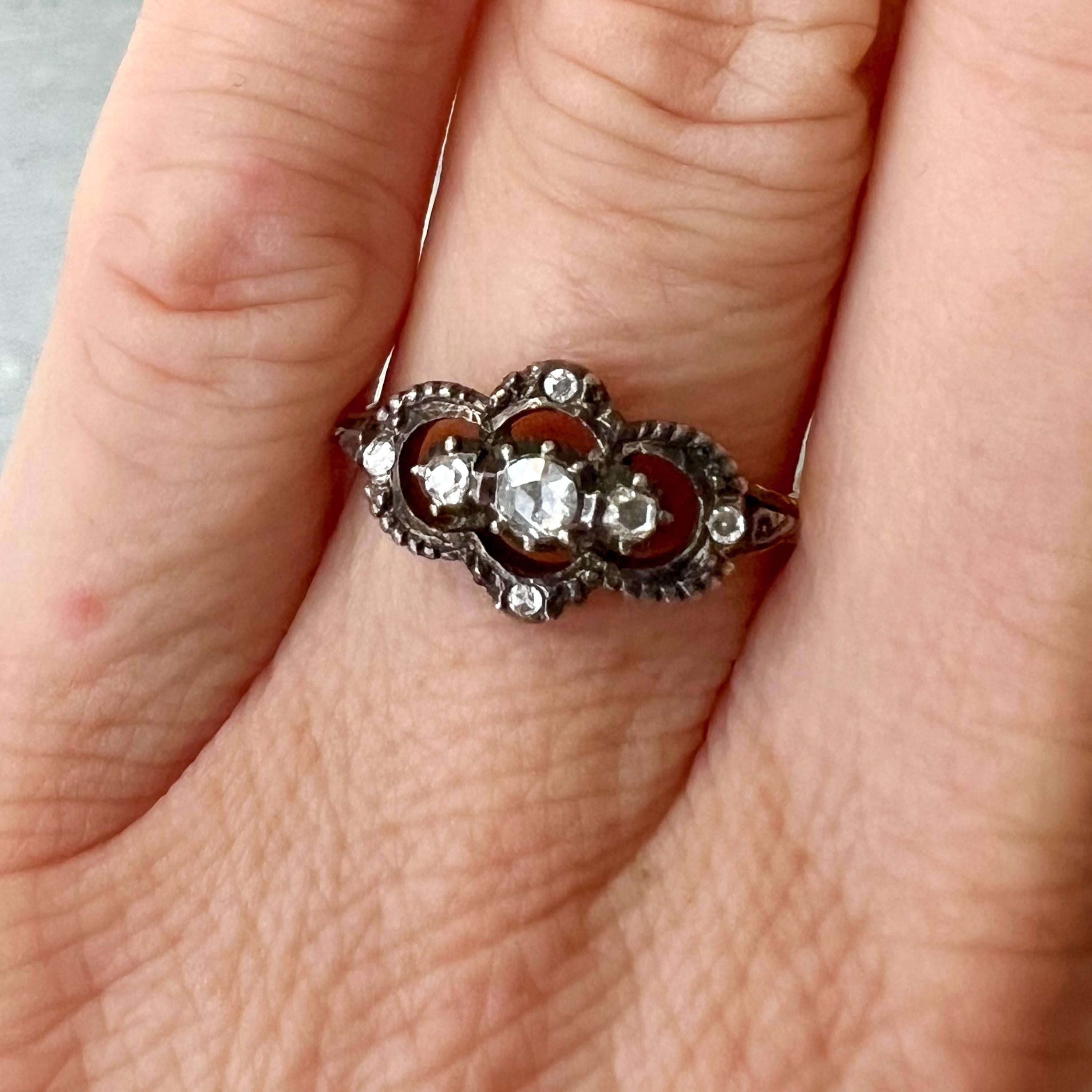 Dieser Ring aus 14 Karat Gelbgold hat eine silberne Frontfassung, die mit 7 Diamanten im Rosenschliff in verschiedenen Größen besetzt ist, die in einer geschlossenen, silbernen, geriebenen Fassung liegen. Der Schaft des Rings ist aus 14-karätigem
