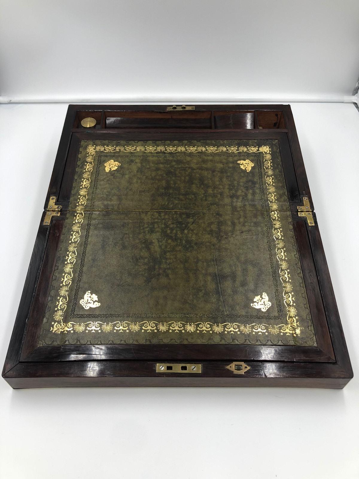 Ancienne boîte à écrire victorienne en bois de rose et laiton, avec un couvercle qui s'ouvre pour révéler une surface d'écriture en cuir vert et un intérieur équipé d'un encrier.
Bon état.