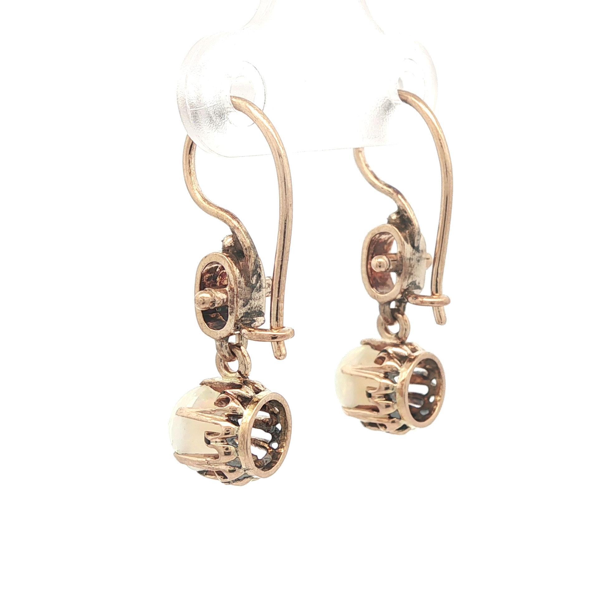 -A. Stone
(2) Opali naturali autentici - taglio cabochon rotondo - incastonati - base bianca con lampi di colore rosso e arancione - 5,9 mm ciascuno (circa)

Materiale: Oro massiccio giallo rosato 14k
Peso: 2.72 grammi
Supporto: Filo metallico con