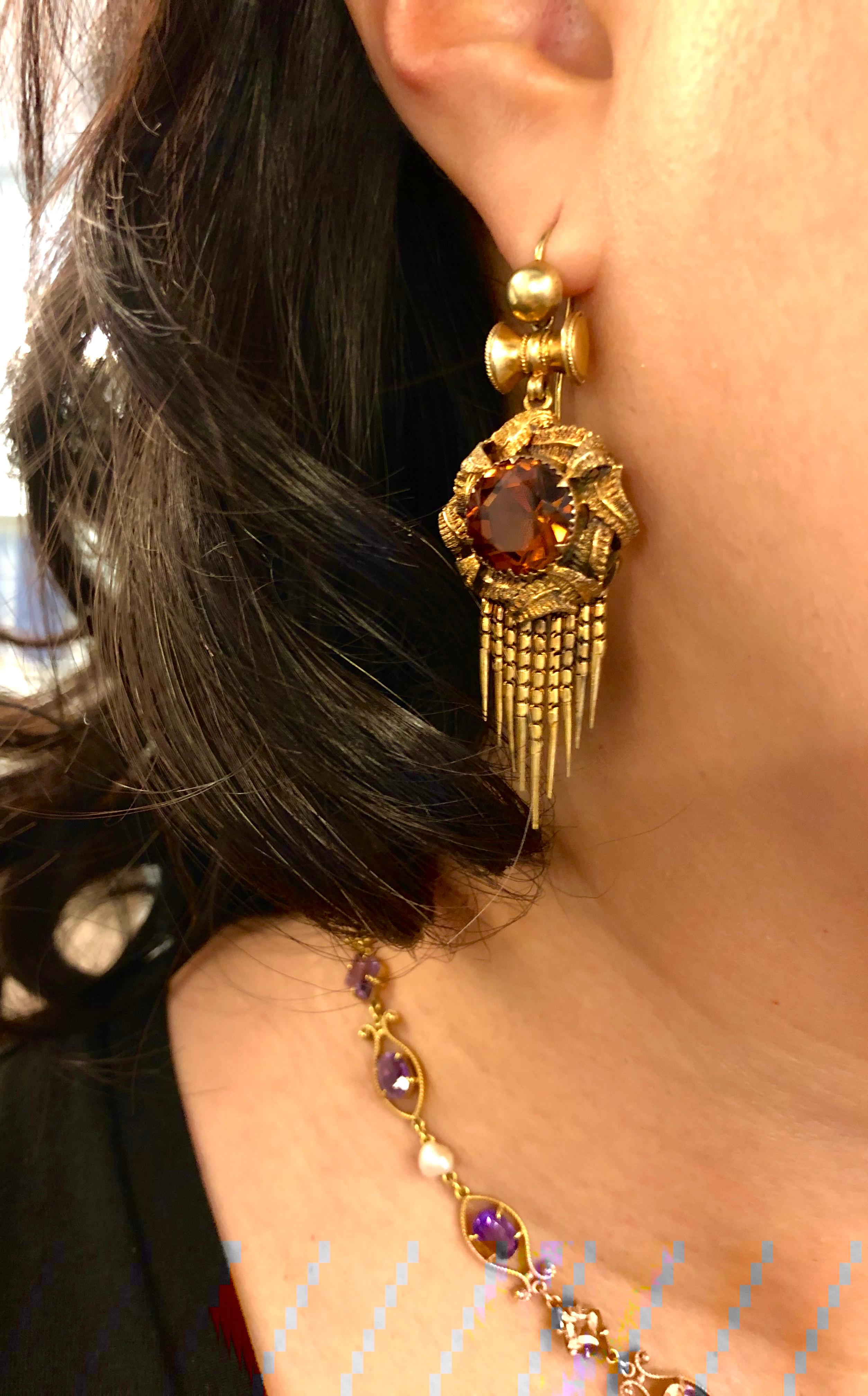A wearable and fun pair of antique Victorian 14k gold citrine pendant fringe earrings. The earrings center upon a round citrine with a golden orange color. The citrine is surrounded by engraved gold leaves and suspend slinky darts of gold chain to