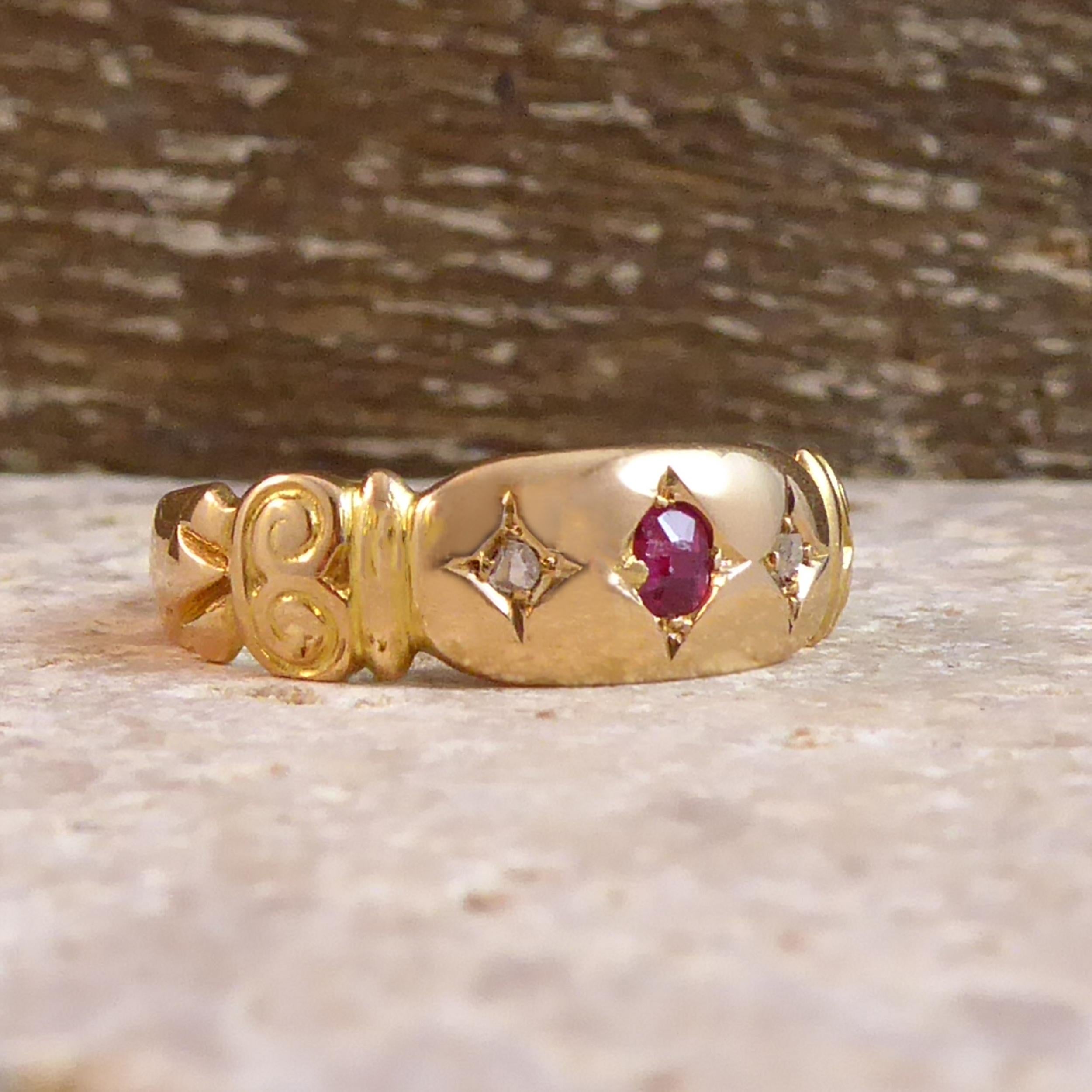 An antique ruby and diamond ring from the English Victorian era.  Set to the centre with a round ruby and an old diamond to each side, these three stones are all bead set to diamond shaped mounts across a slightly bevelled gold plaque with grooved