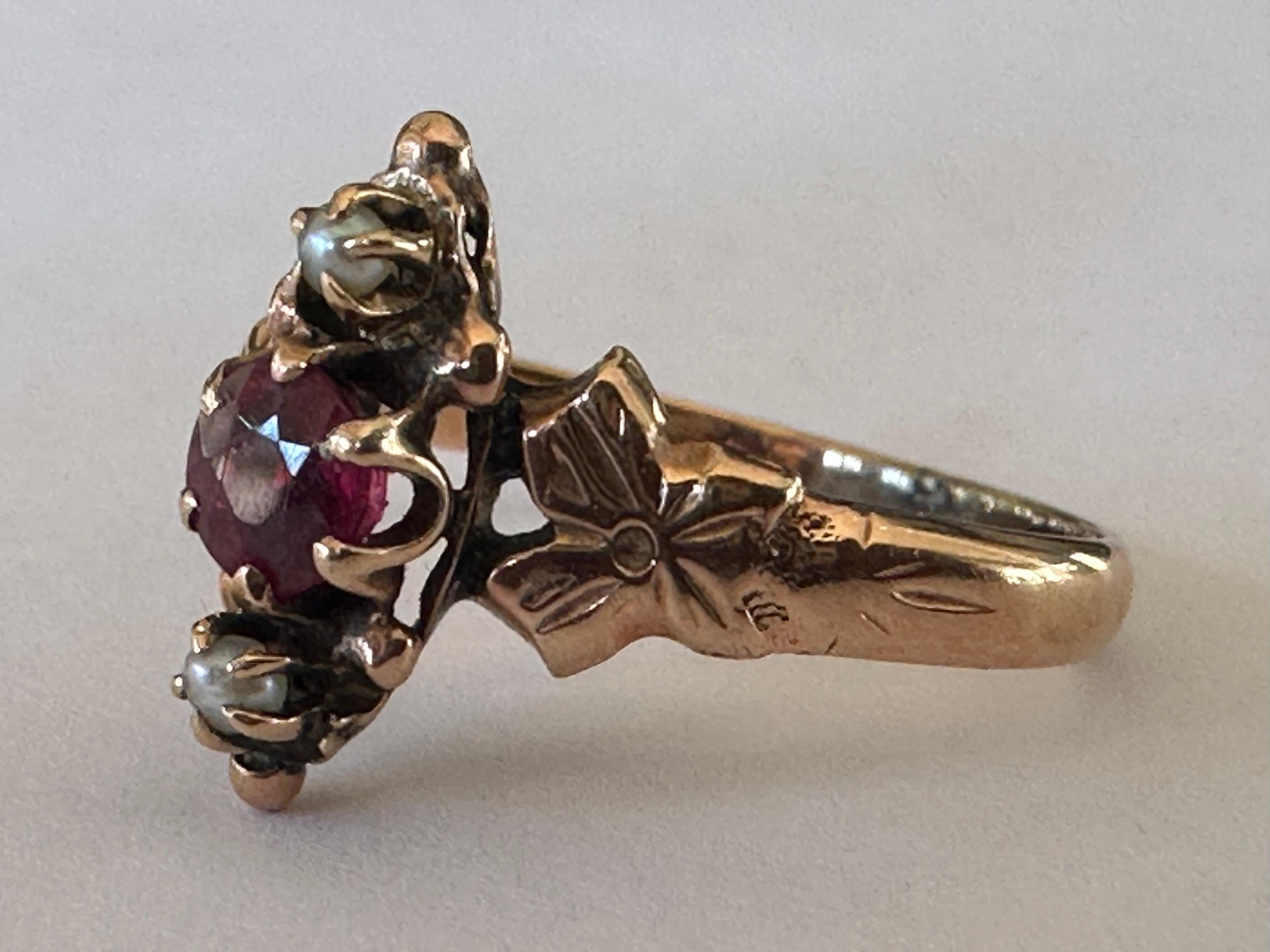 Crafted in the late nineteenth century, this antique Victorian ring is designed around an approximately 0.25-carat ruby and accompanied north and south by two seed pearls and ornately engraved flowers. Set in 10K rose gold. 

