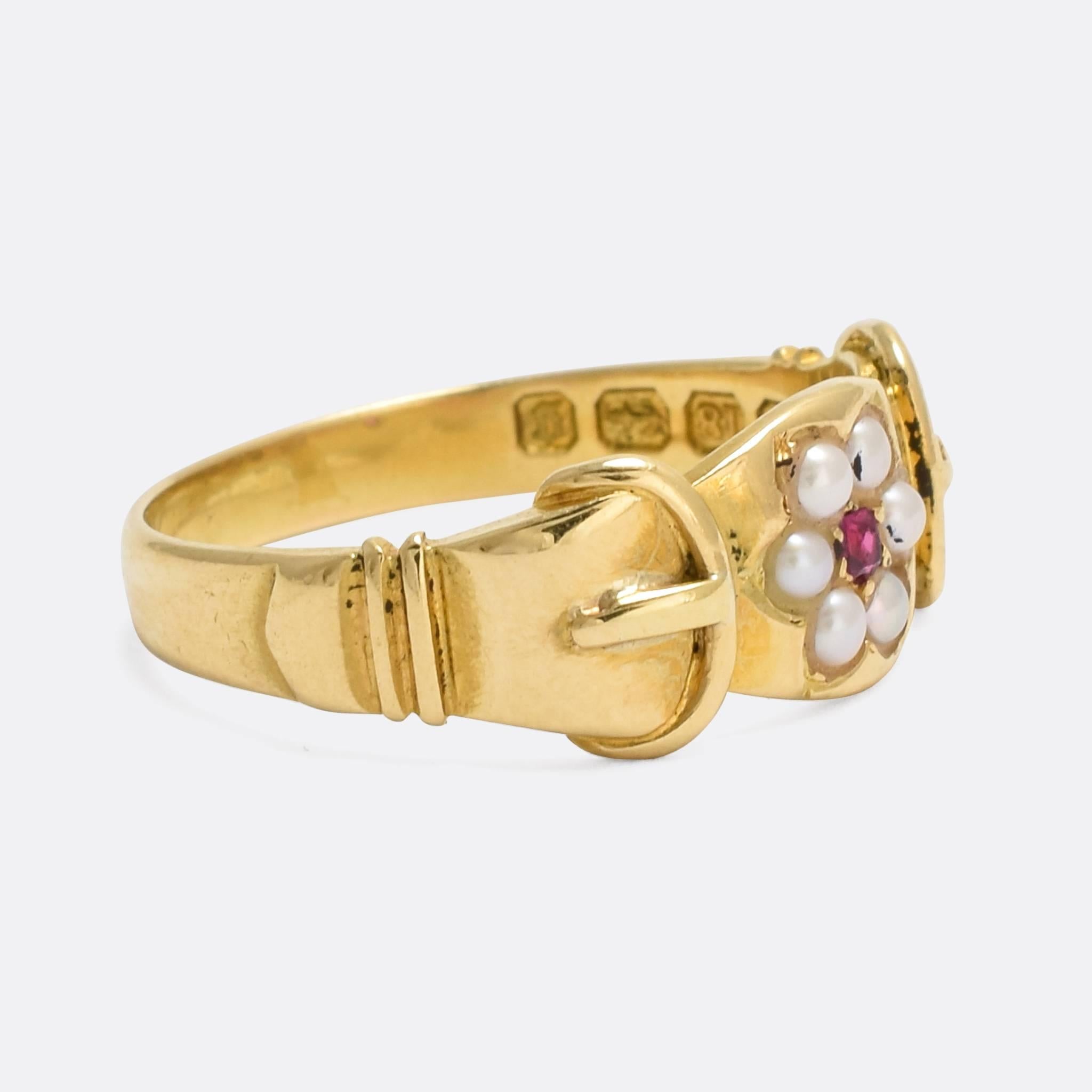 A pretty antique cluster ring set with a natural ruby surrounded by a halo of pearls. The shoulders are modelled as buckles, and the stones set into a flower motif. It's crafted from 18k gold throughout, with clear English hallmarks dating to the
