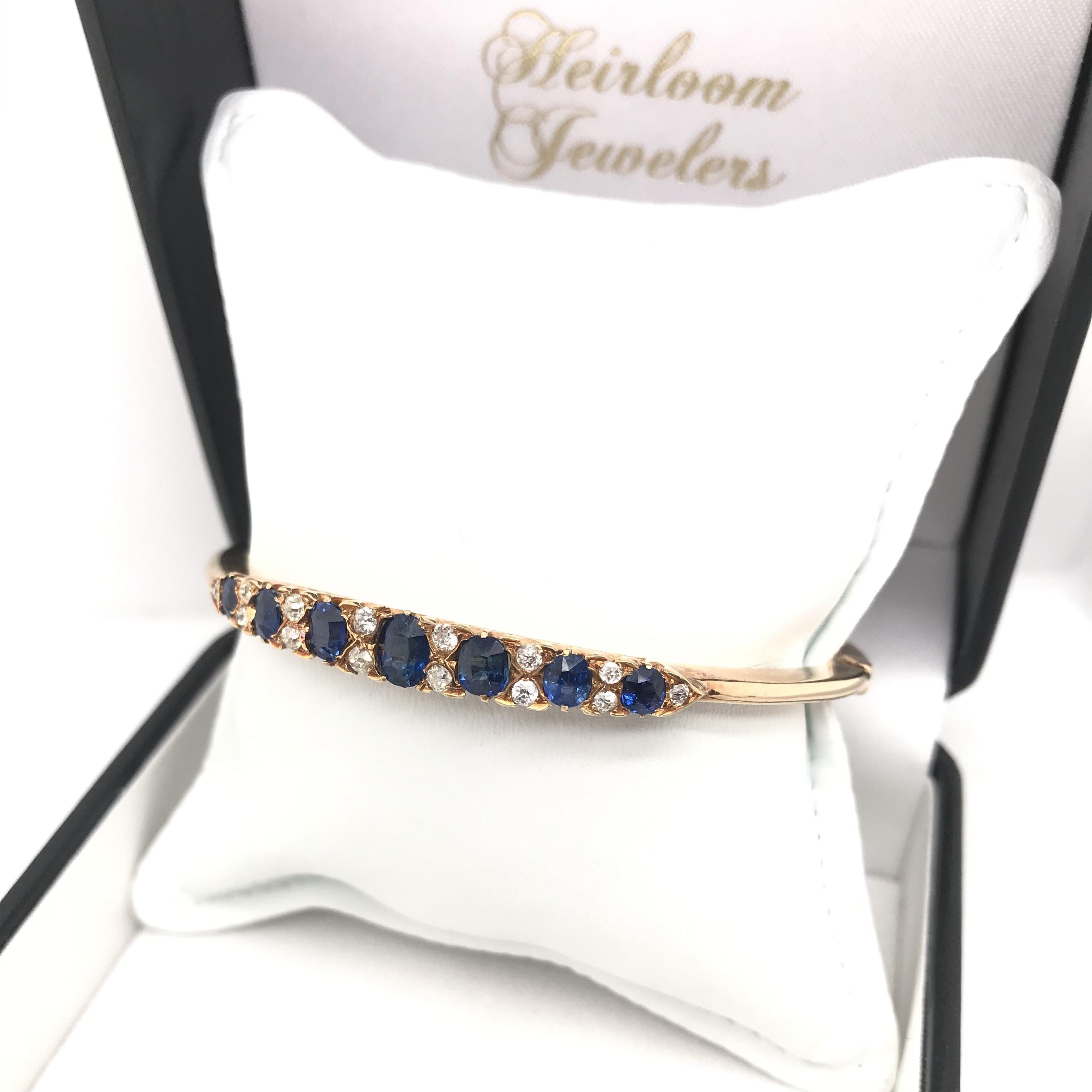 This antique bangle bracelet was crafted sometime during the late Victorian design period (1840-1900). The 18K gold setting features seven richly hued and antique oval cut blue sapphires. The sapphires have been certified by the Gemological