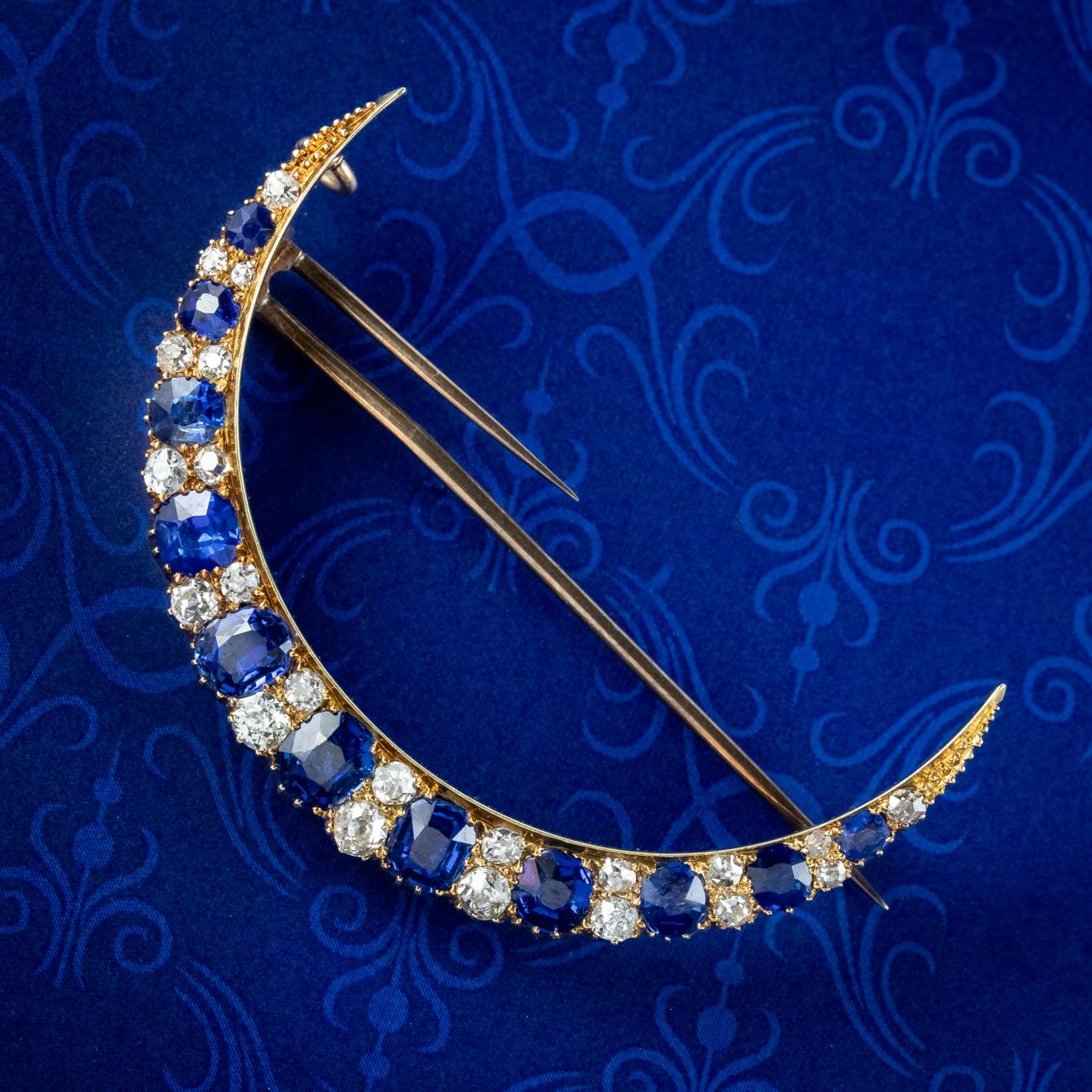 A stunning antique Victorian crescent moon brooch from the late 19th Century adorned with alternating cushion cut blue sapphires and old mine cut diamonds that graduate in size toward the centre. The sapphires have a beautiful royal blue hue and