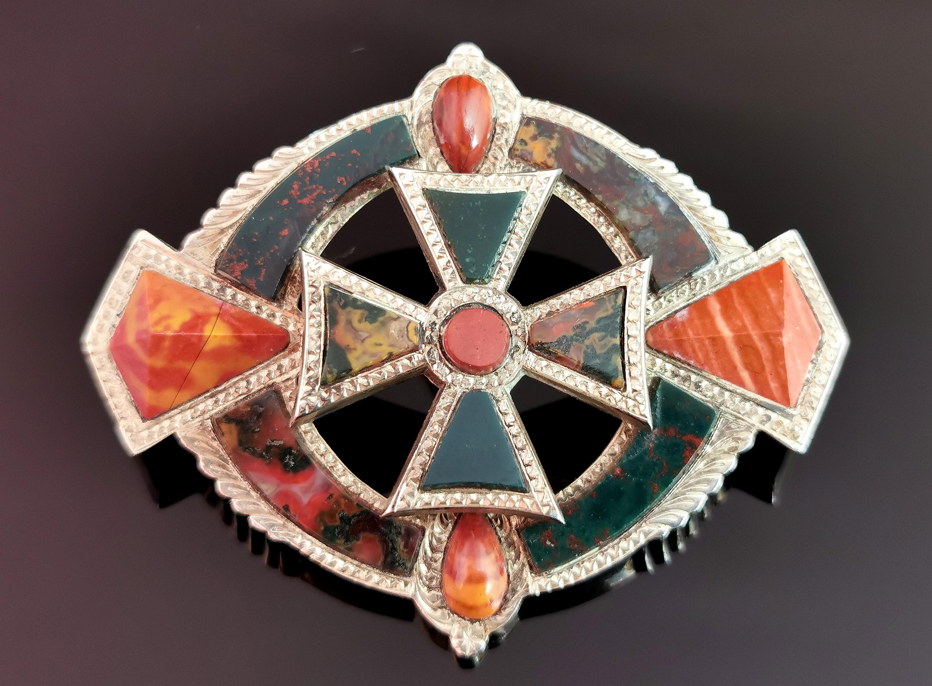 A gorgeous and grand antique, Scottish agate and Silver brooch.

It has an oval shape set with diamond shaped carved red Jasper each end and a tear drop cabochon top and bottom, a very interesting design.

The centre has a celtic cross set with