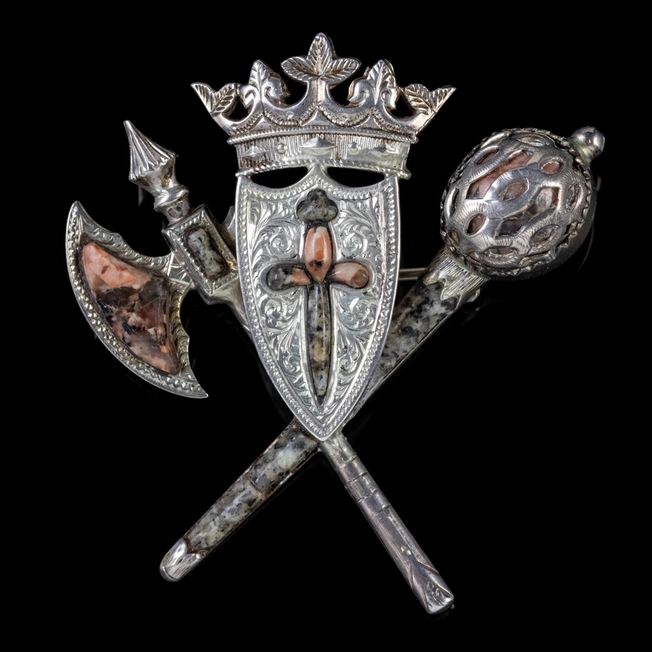 A wonderful Antique Victorian Scottish brooch featuring an engraved shield adorned with a sword, topped with a crown with a crossed axe and sword behind. 

Scottish Granite stones have also been cut and placed to decorate the brooch and have lovely
