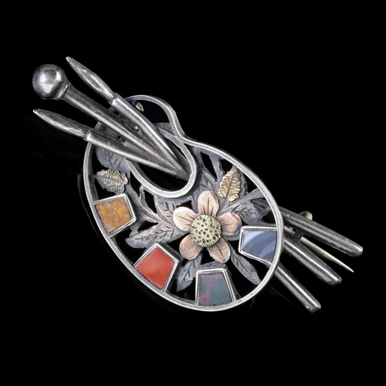 A unique Antique Victorian Scottish brooch modelled in solid Silver, depicting a wonderful paint palette decorated with Golden flowers and brushes threaded through the middle.

Four sections of Scottish Agate have been set in the palette rather