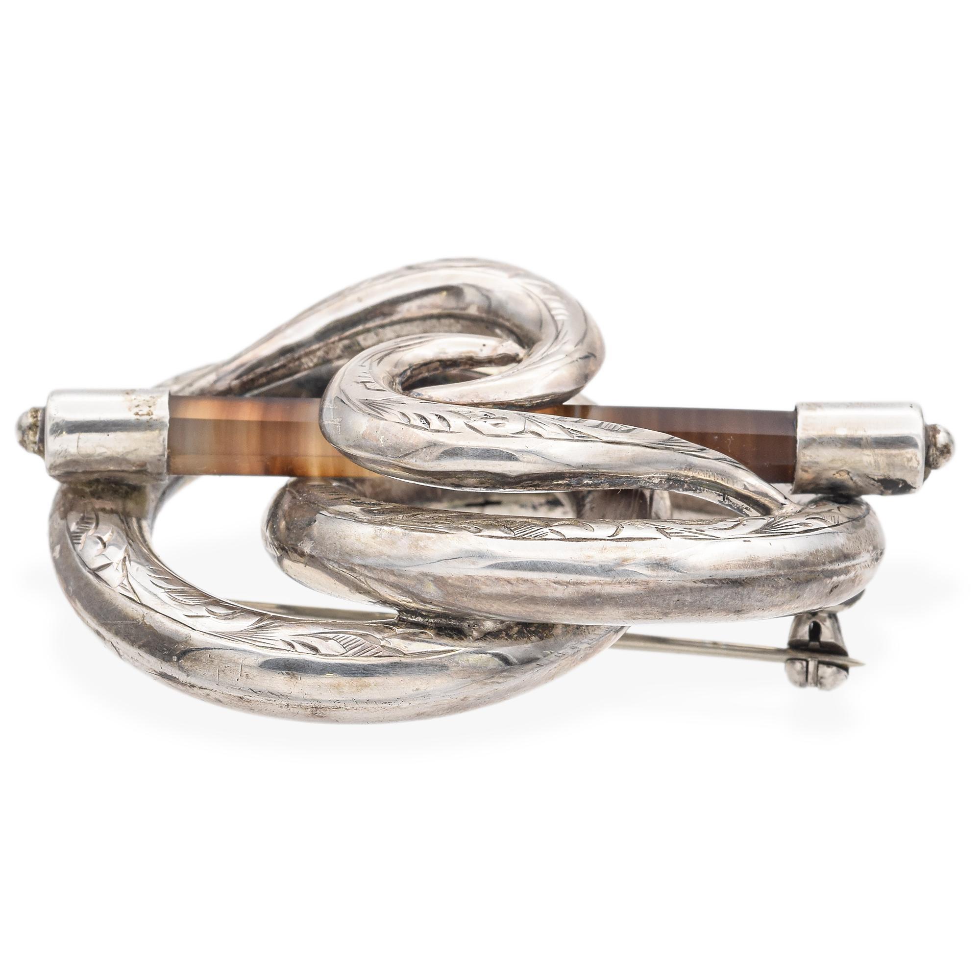 A Victorian brooch from 19th century Scotland, featuring an intricate knot design. The piece showcases a brown hexagon-cut agate, elegantly set in silver showcasing elaborate engravings. The Lover's Knot, a popular motif in the Victorian era, often