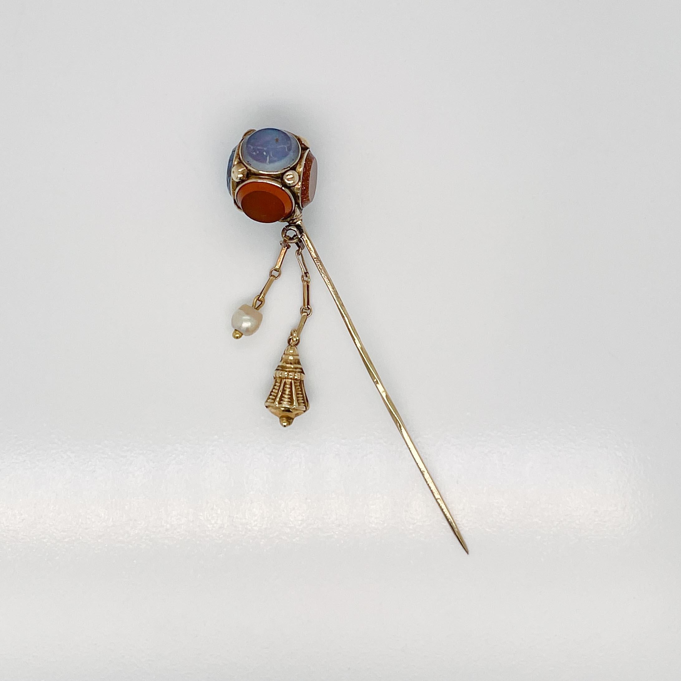 A fine Victorian Scottish stickpin.

With flat, round agate cabochons bezel set in 14k gold cube-shaped top.  

A decorative gold charm and pearl are suspended from the top. 

The pin shaft has a little twist in center of pin.

Simply a eye-catching