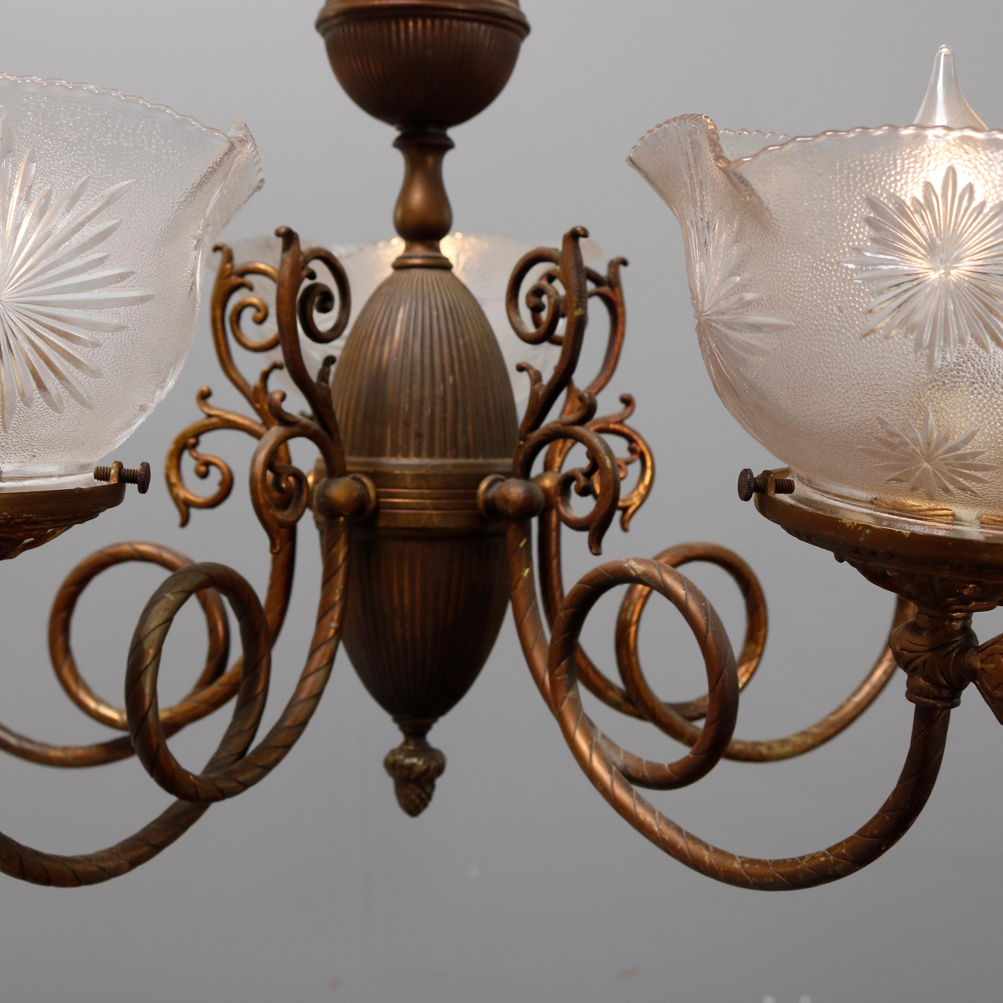 An antique Victorian electrified gas chandelier offers brass construction with urn form font with acorn drop finial and having five scroll arms terminating in candle lights with ruffled rim glass shades, circa 1890

Measures: 26