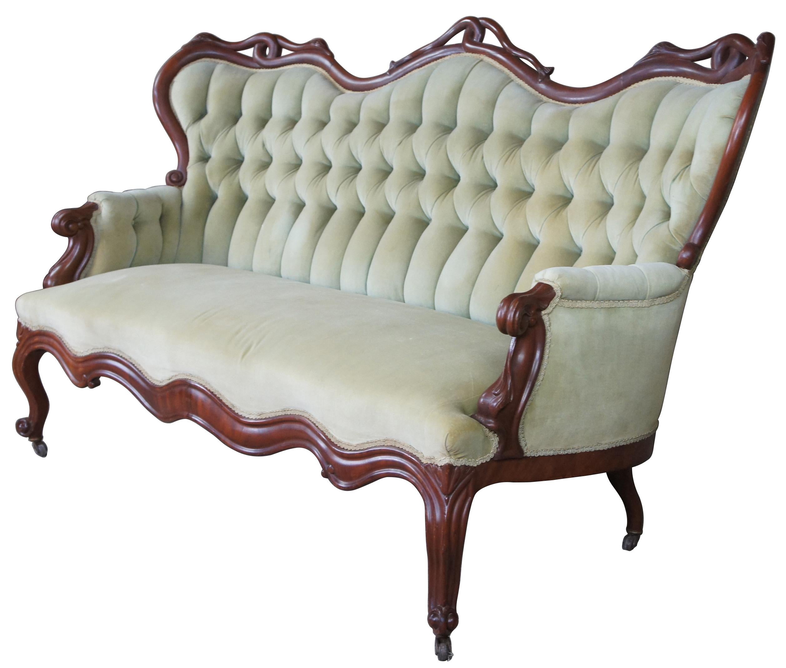 Antique Victorian carved parlor sofa or settee. Made of mahogany with serpentine form featuring carved intertwined serpents with swan like heads and fish tails along the wingbacks and tufted suede upholstery. Measures: 75