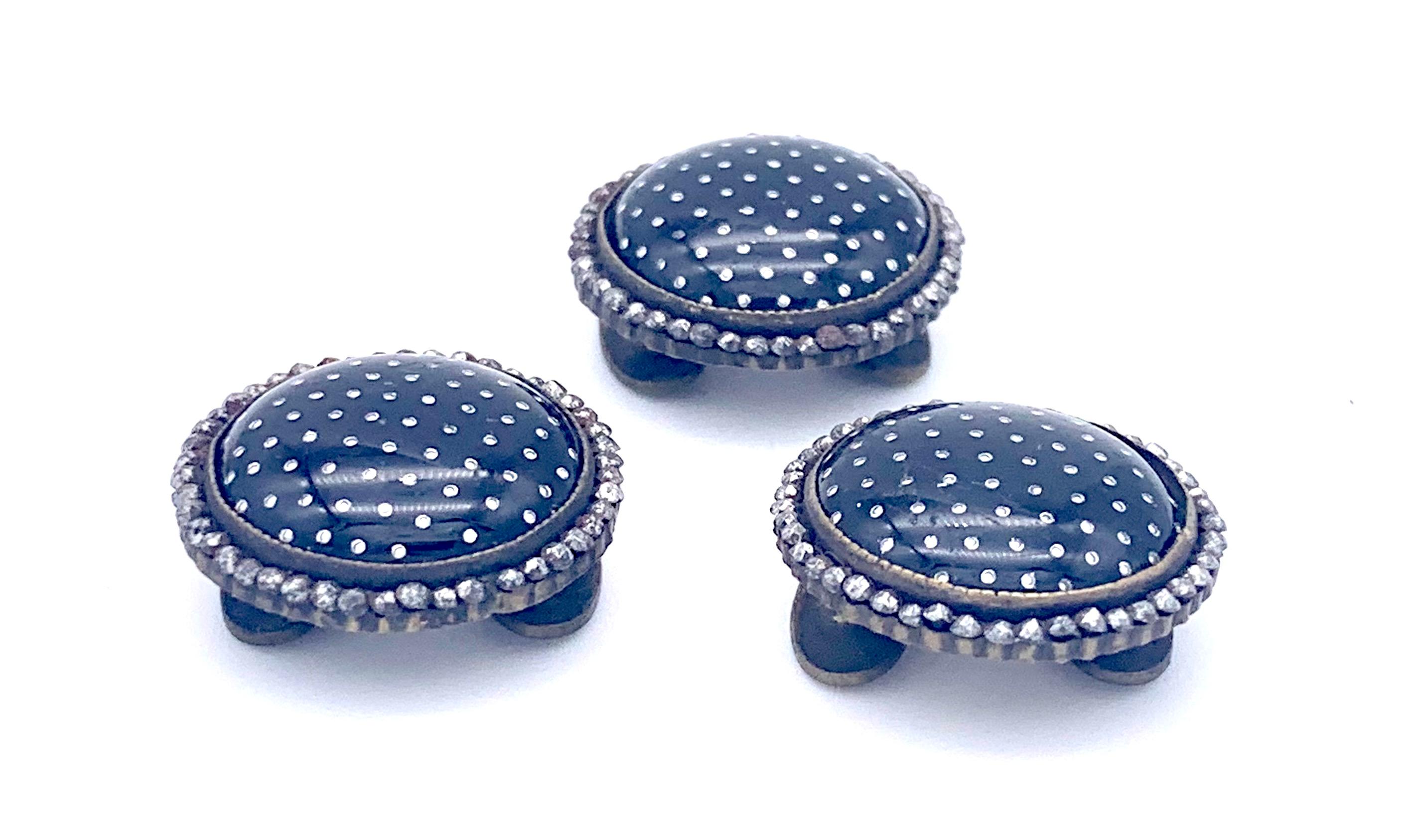 These Victorian buttons were created in the middle of the 19th century out of brass. Each button is decorated with a rim made out of cut steel. The center of each button is made out of metal covered in black enamel and decorated with white