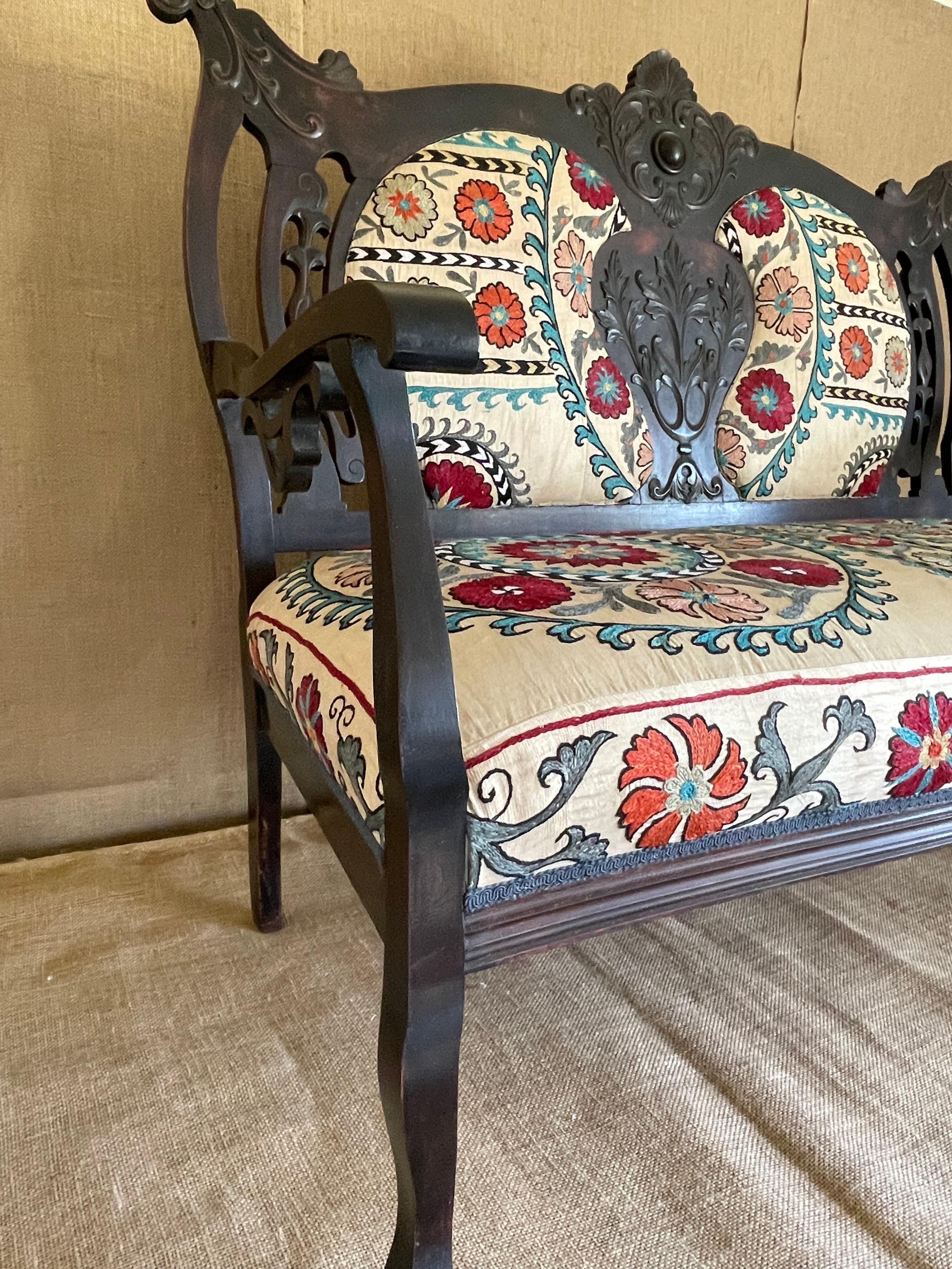 This love seat is made of carved mahogany in the Victorian style and has been reupholstered with a beautiful Antique Uzbek Suzani textile. The carved frame highlights the rich mahogany wood, while the exquisite textile adds a touch of elegance and