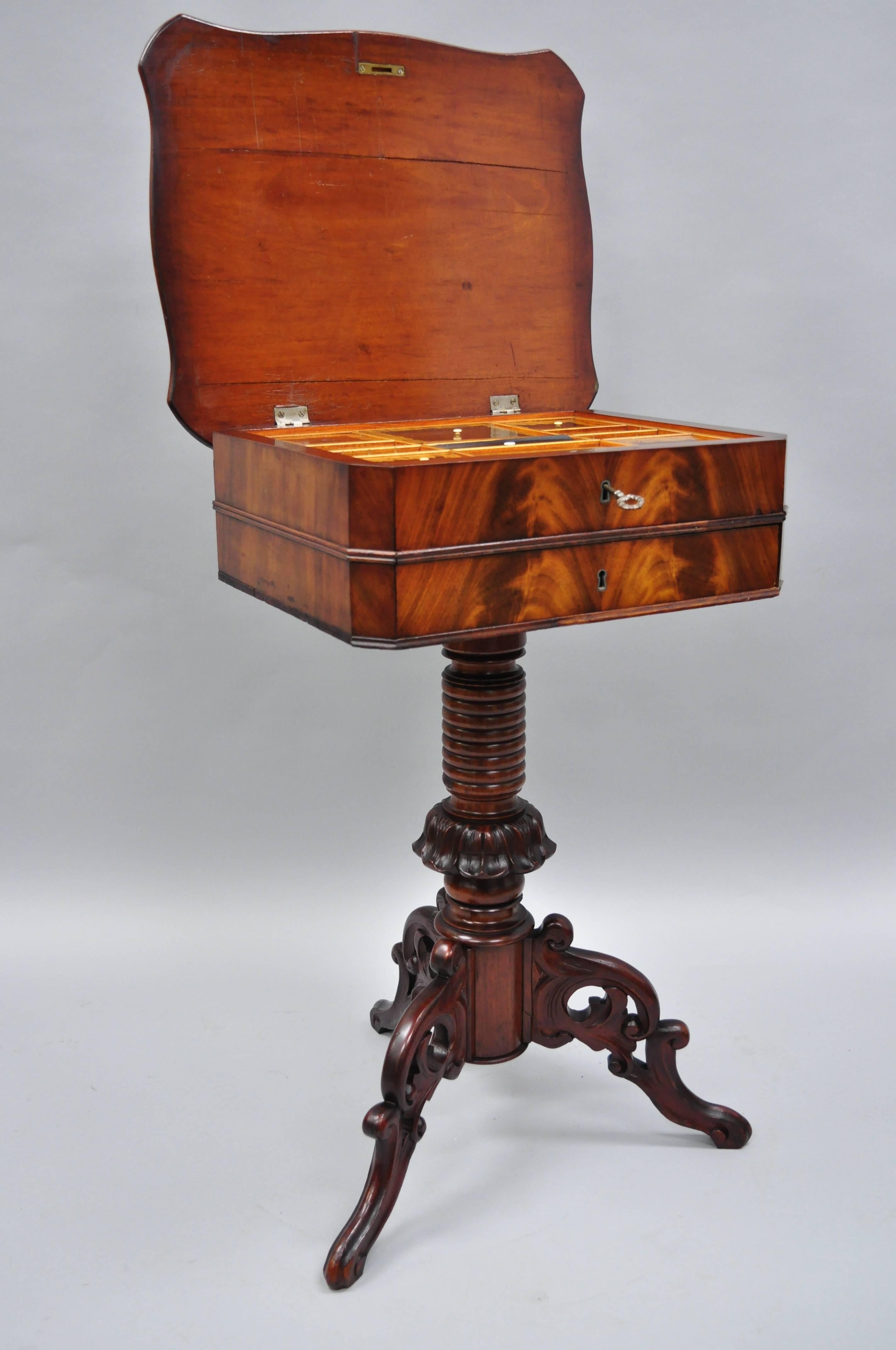 Antique Victorian sewing stand side table in crotch mahogany and walnut. Item features a crotch mahogany banded top, ornately carved tripod pedestal base, beautiful wood grain, finely carved details, working lock and key, two dovetailed drawers.