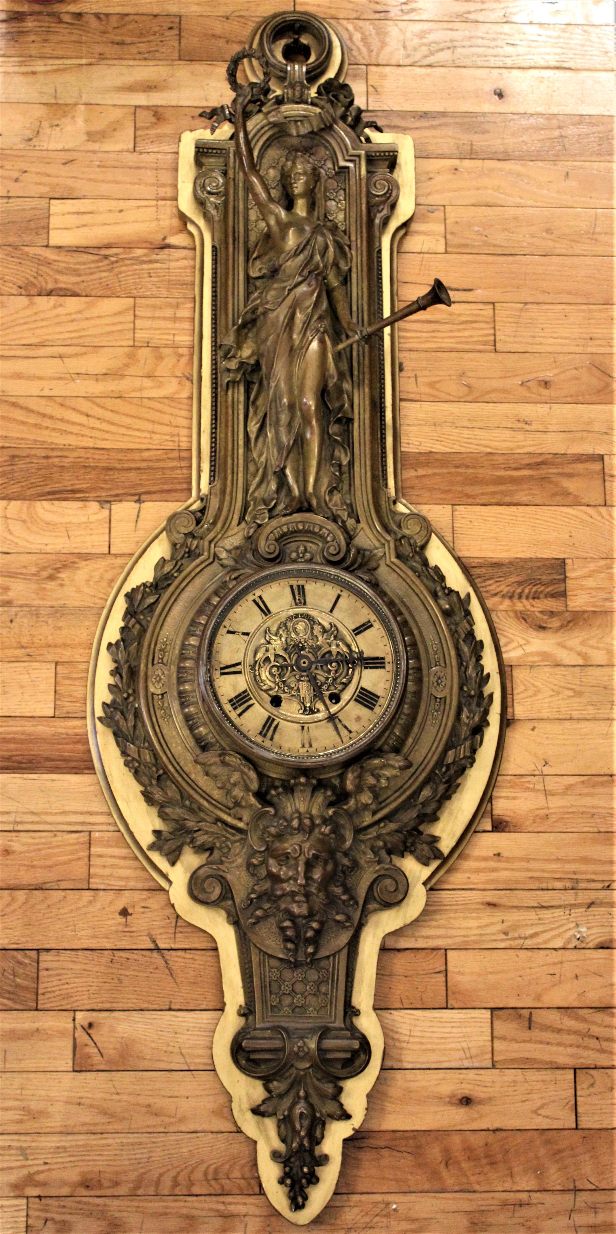 Pendule murale française en bronze massif de style victorien, signée Tiffany & Co., dont le boîtier en bronze coulé représente une jeune fille tenant une couronne d'une main tendue et une trompette dans l'autre. Sous le mouvement de l'horloge se
