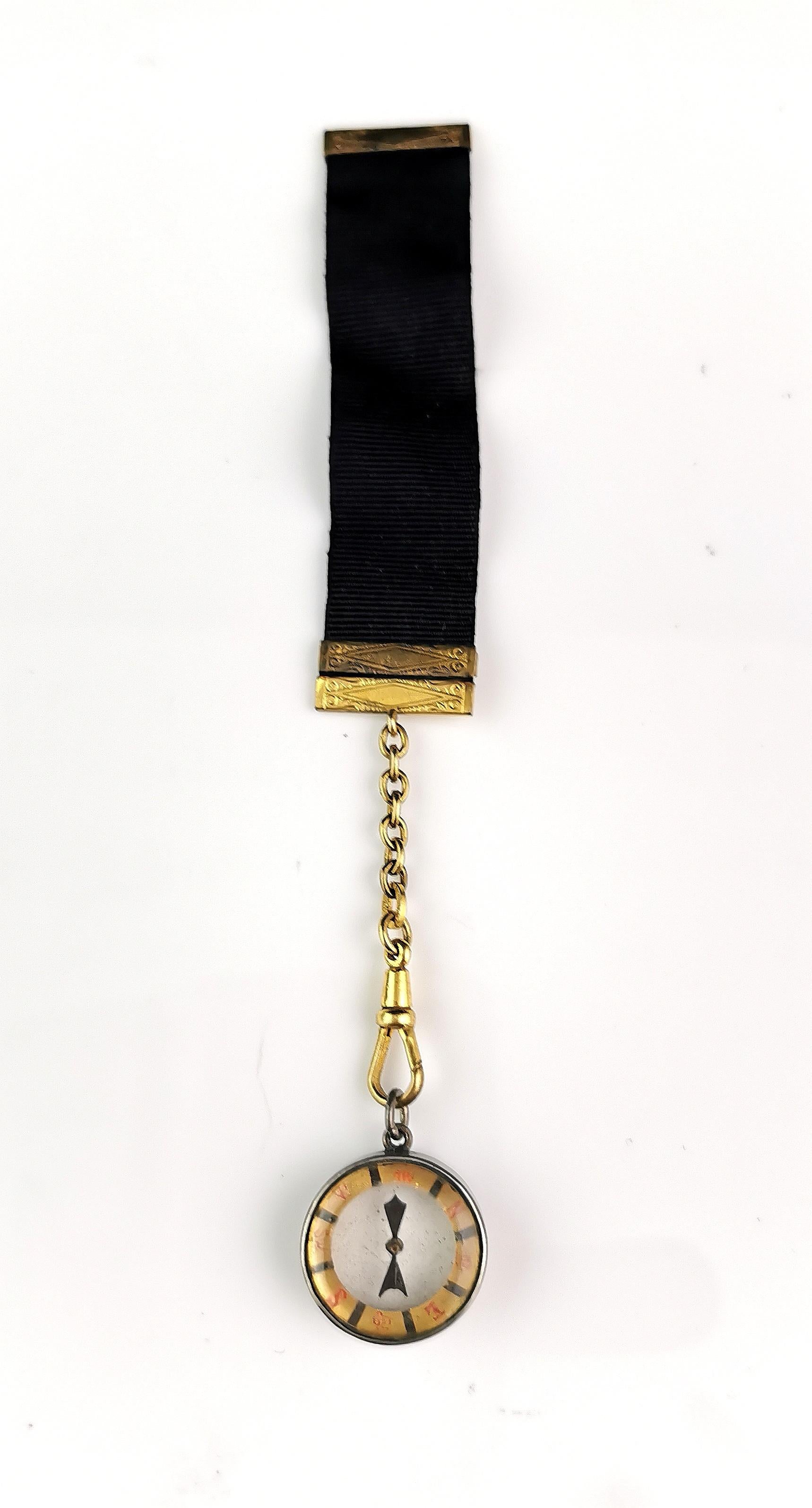 A lovely antique Victorian era black silk ribbon fob with a gilt compass.

The long black silk fob is sleek with rich gilt end caps and a chain length suspended from the bottom.

There is a small gilt metal compass attached to the chain length by a