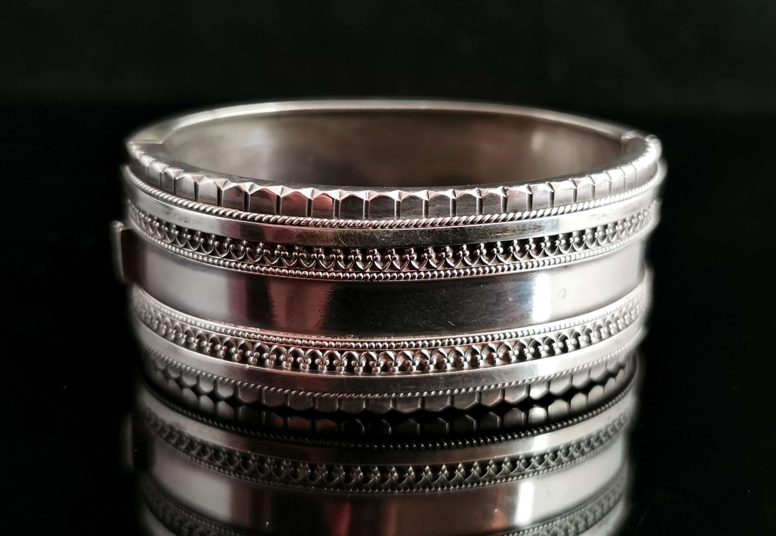 A beautiful antique Victorian era sterling silver bangle.

A wide bangle, almost an inch wide with a day to night design, one side finished in a plain polished silver and the other side with gorgeous applied scrolling arches and beading.

The edge