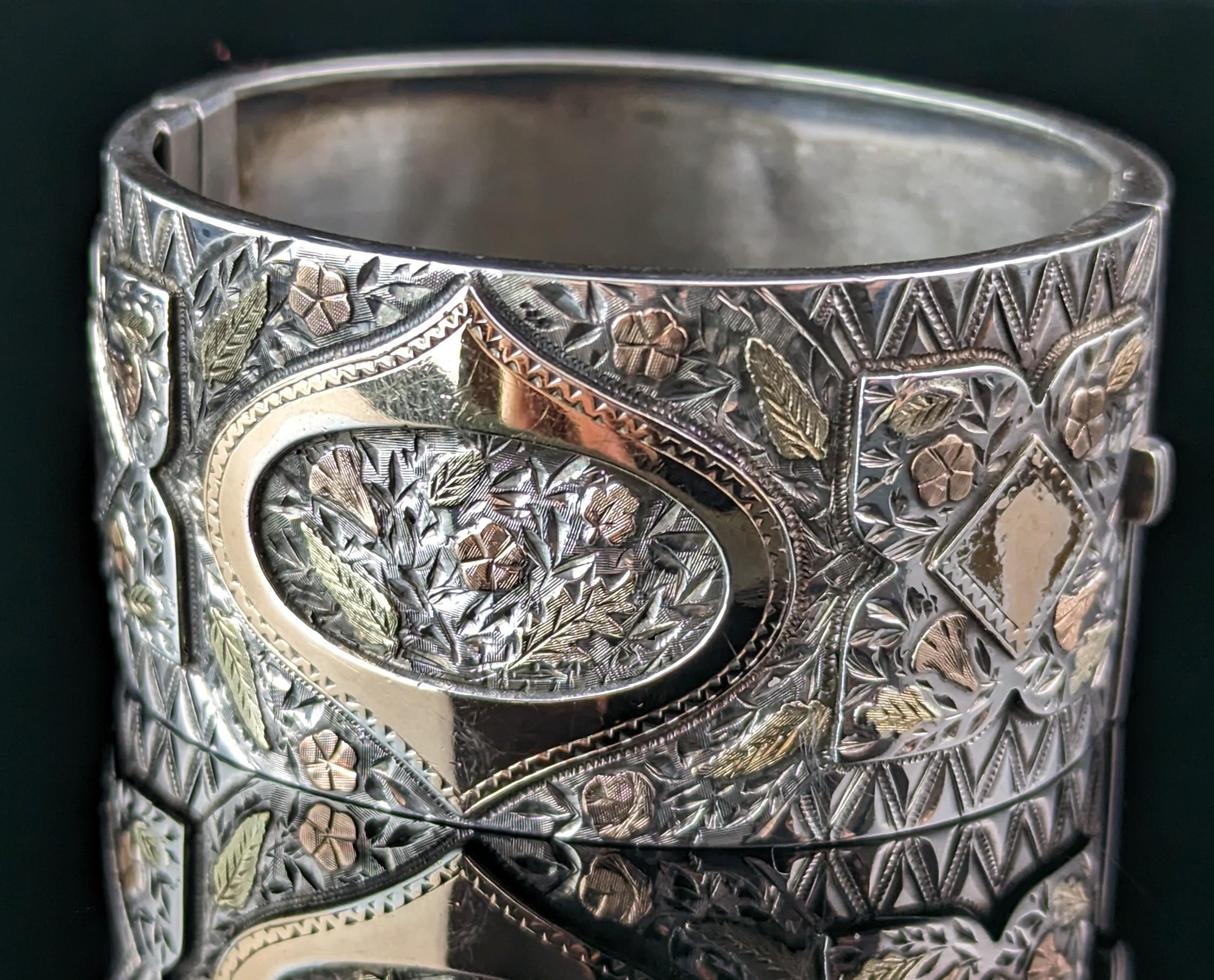 You can't help but fall in love with this gorgeous antique, Victorian, sterling silver and gold bangle.

The bangle is wide and chunky with a smooth polished reverse and a profusely engraved front with areas picked out in relief and beautiful