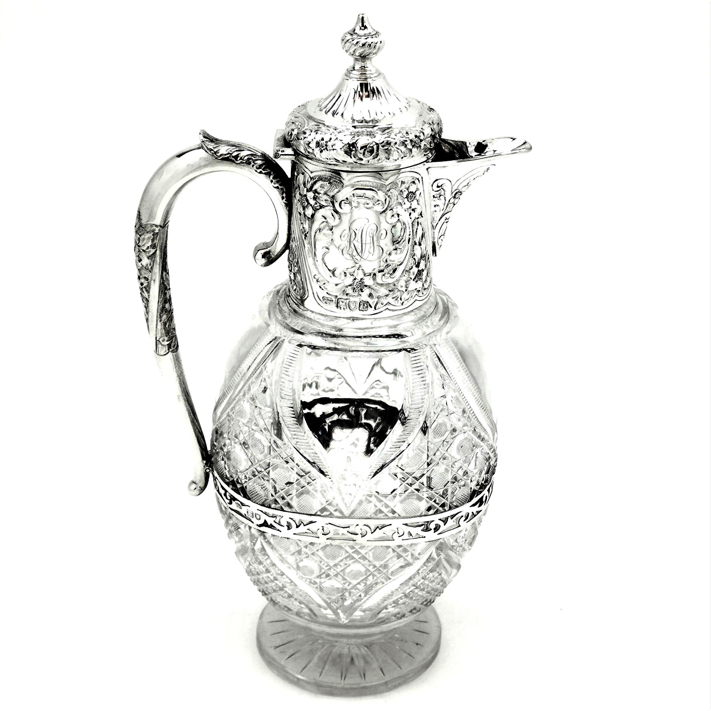 An elegant antique Victorian silver mounted cut glass Claret Jug. This Wine Jug has a cut glass body and a solid silver neck, handle and hinged Lid. The collar of the Jug has a delicate floral pattern chased around the exterior mirrored on the