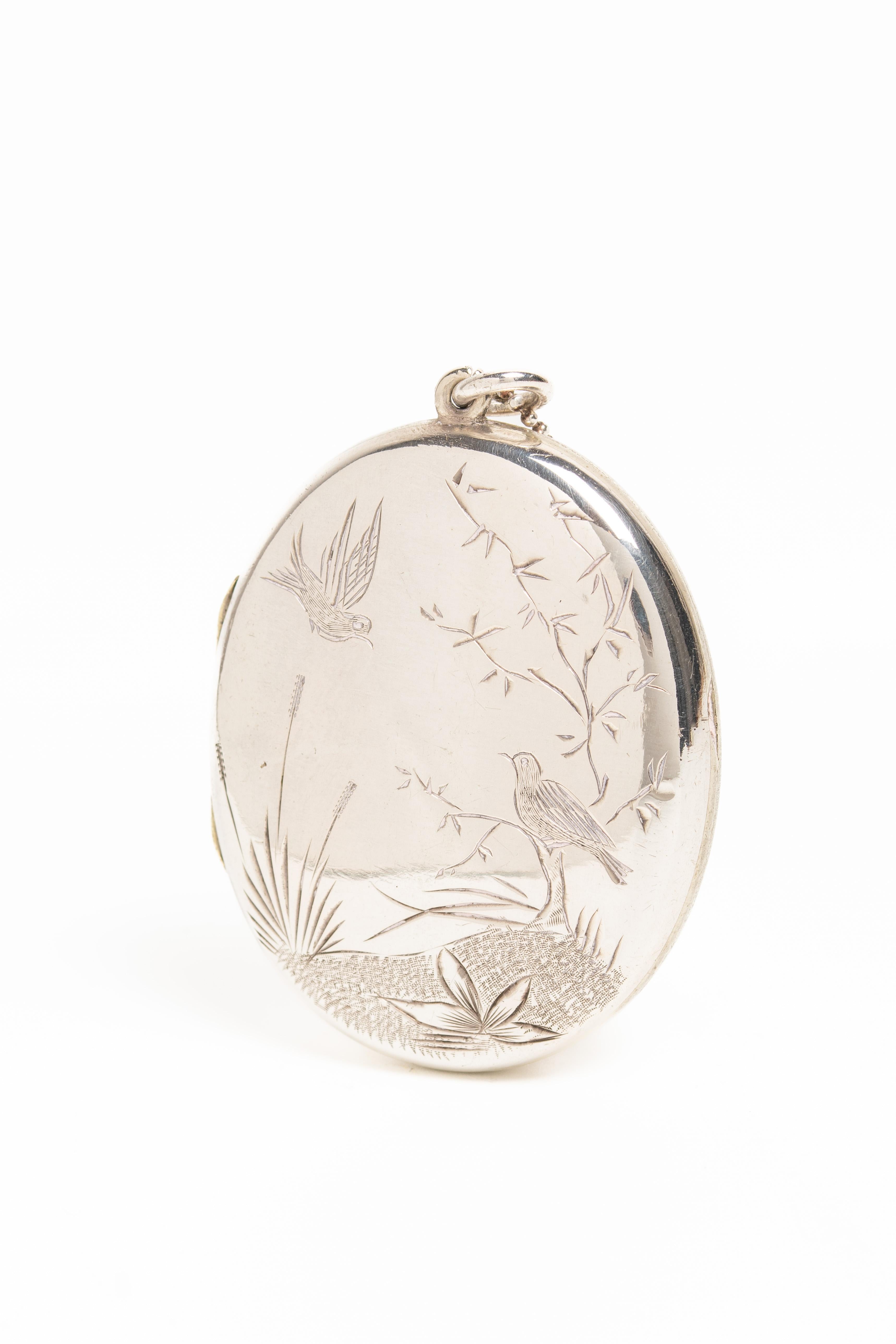 Beautiful Victorian silver locket in the Aesthetic Movement style circa 1890. The front of this locket depicts a pair of love birds, one in a flight and another one sitting on the tree branch. The love birds were a very popular symbol in the