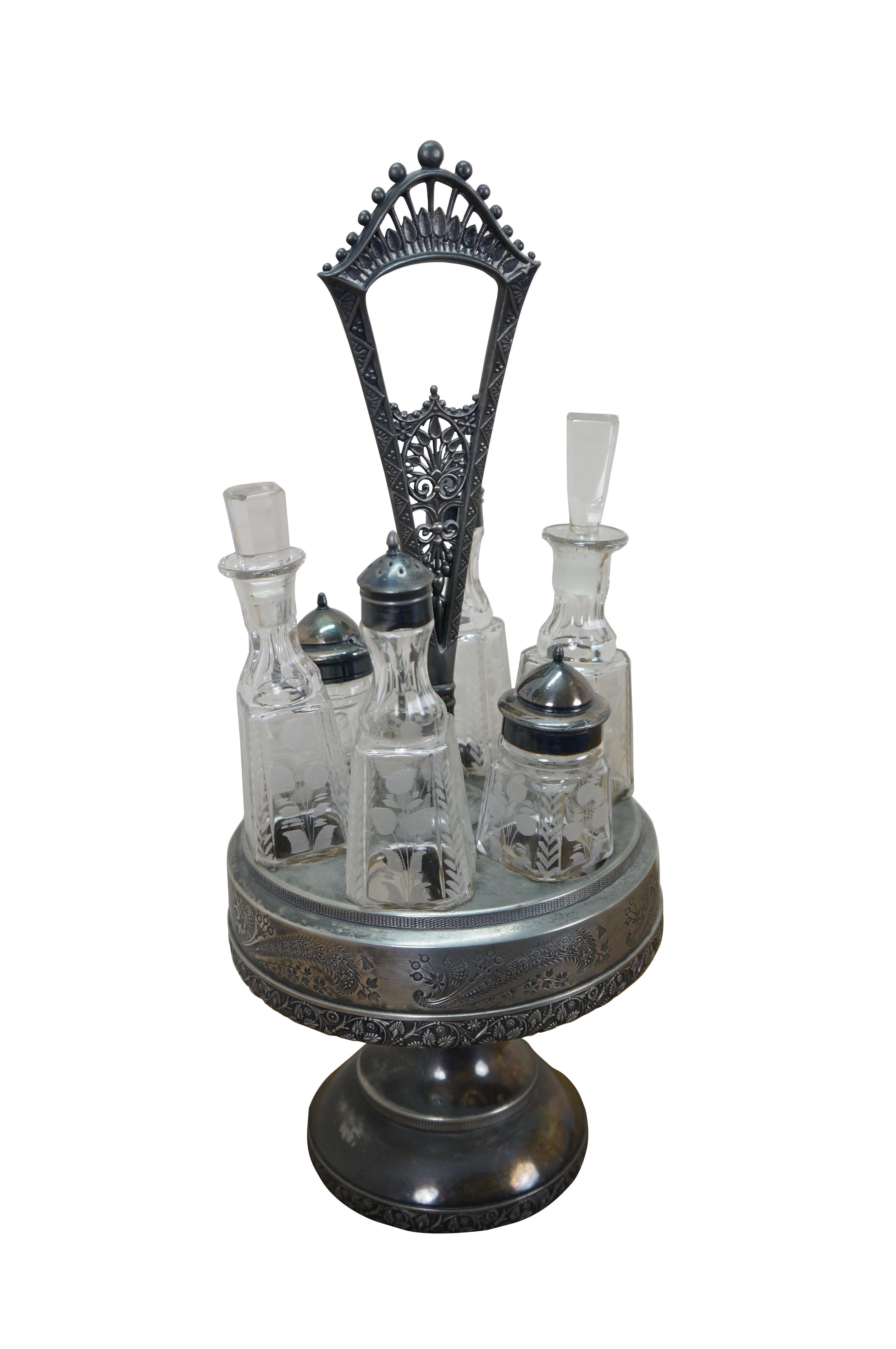 Antico set di ampolle repousse da sette pezzi. Lazy Susan rotonda / piedistallo girevole decorato con tralci floreali e ramoscelli di paisley e una maniglia traforata con foglie al centro. Contiene un set di sei bottiglie in vetro inciso a fiori e