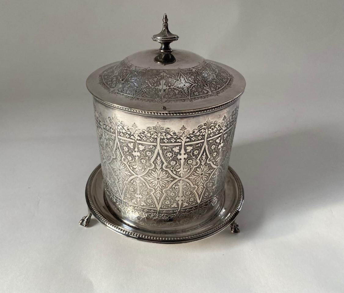 Das antike viktorianische runde Biskuitfass aus Silberblech ist ein charmantes und elegantes Stück, das das Designempfinden der viktorianischen Ära widerspiegelt. Dieser exquisite Behälter ist aus versilbertem Material gefertigt und hat ein
