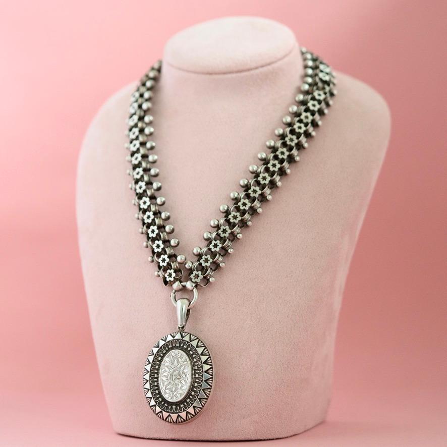 This Antique Victorian Silver Locket and Collar Necklace, hallmarked in Birmingham in 1883, is a magnificent example of Victorian design and symbolism. The sterling silver locket features an ornate front decorated with ivy, dots, and