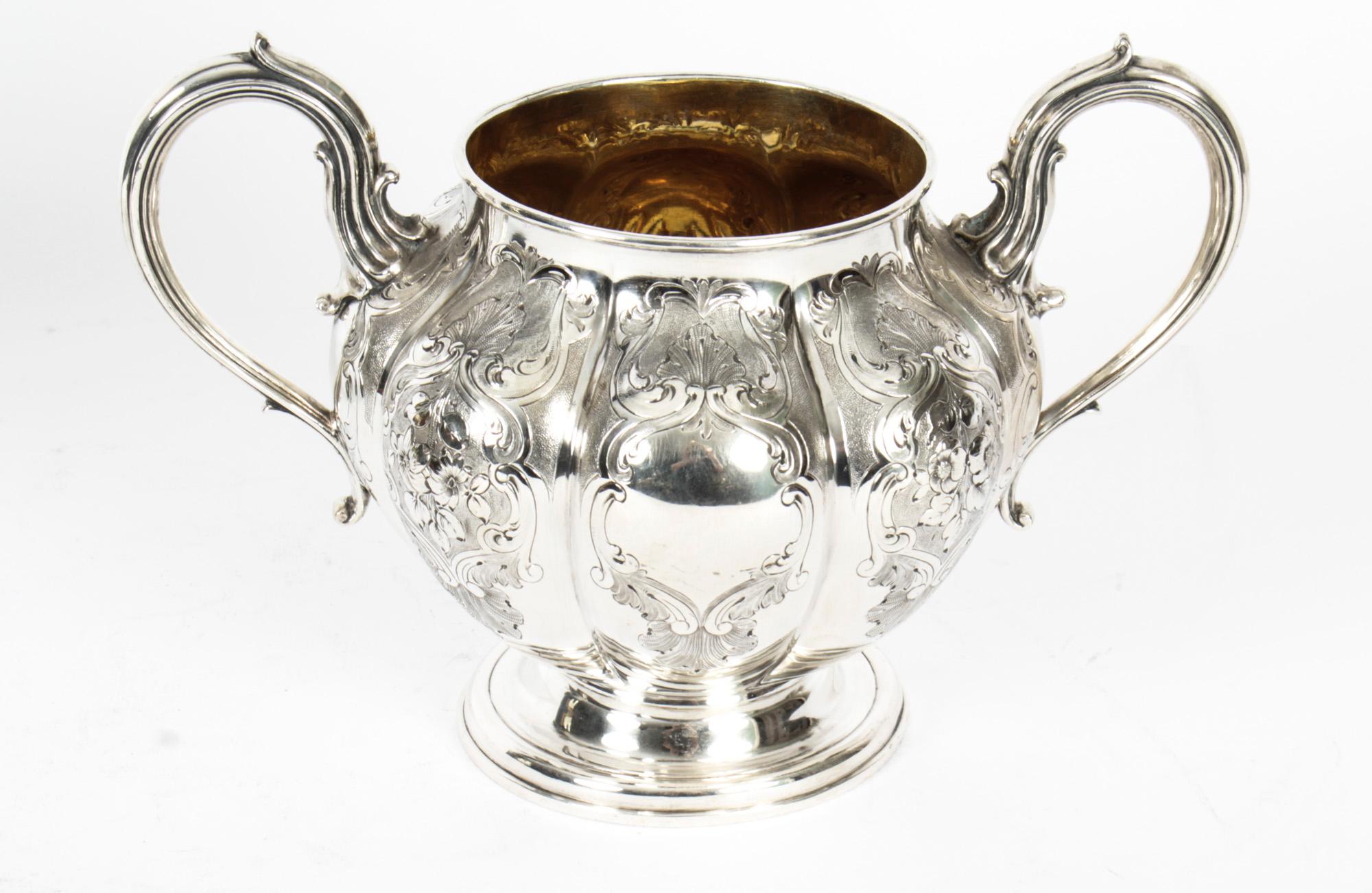 This is a wonderful English Victorian antique silver plated two handled sugar bowl by the world famous silversmith Elkington & Co, with the date mark for 1857.
 
The melon-shaped body features scrolling floral decoration leaf-capped scroll