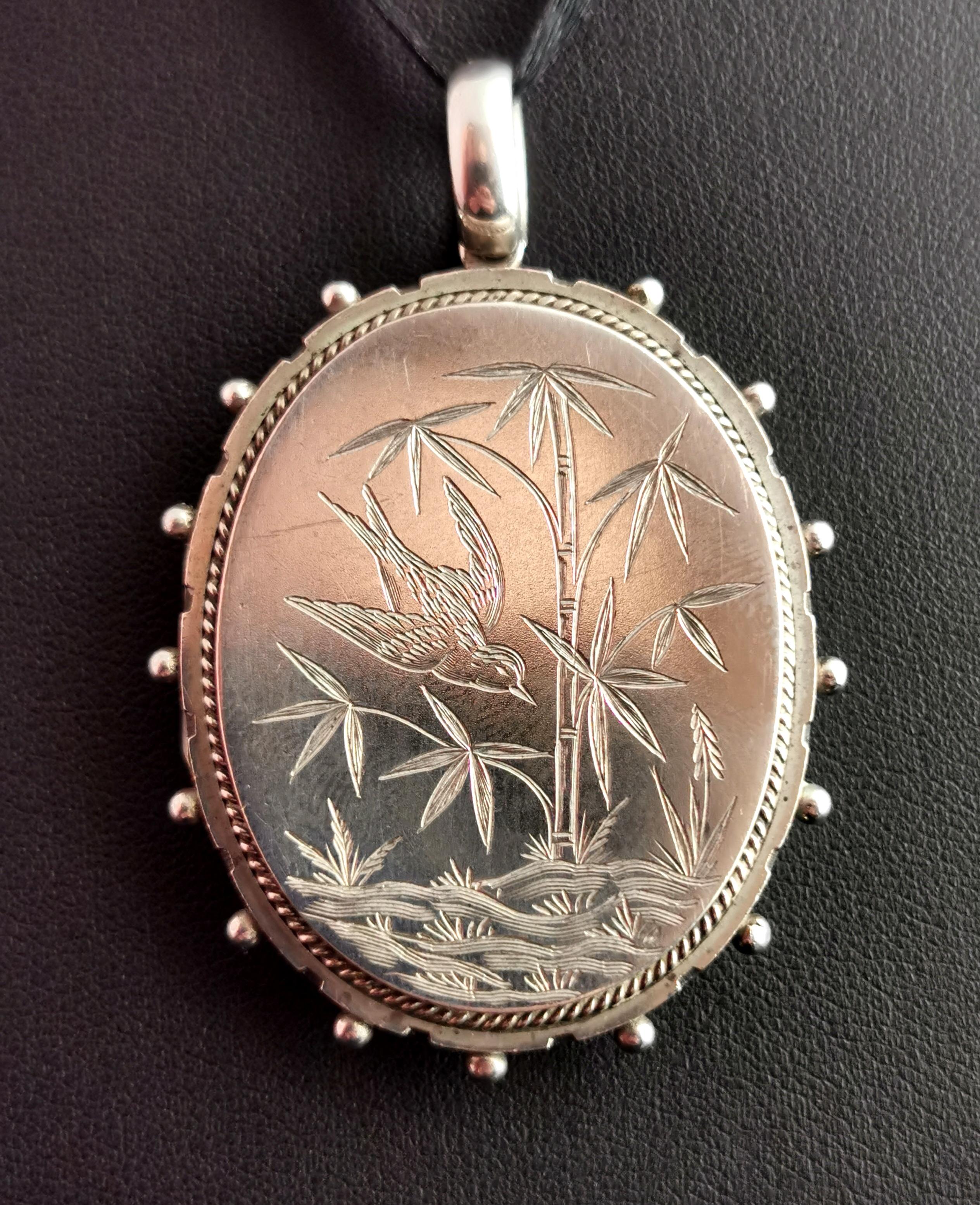 A stunning antique Victorian sterling silver locket pendant.

A large sized oval locket with a beautiful engraving of a Swallow in flight with bamboo and grasslands in the aesthetic manner.

The locket has a smooth reverse and a beaded outer