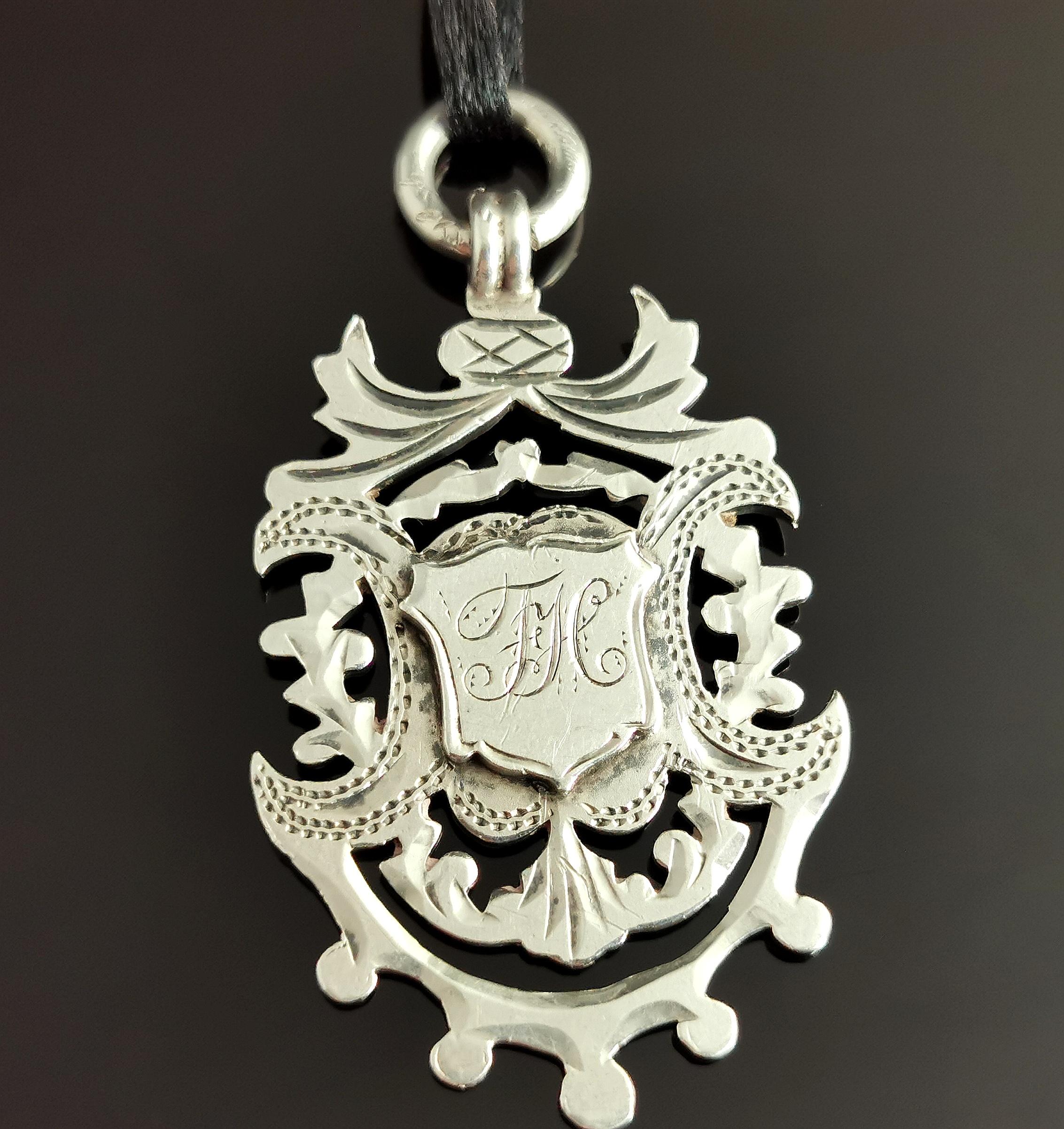 An attractive and elaborate antique sterling silver fob pendant.

A larger fob with a good weight to it, it is a shield shaped piece with a chased, engraved cut out border and a thistle type design to the top.

The fob has a large silver jump ring