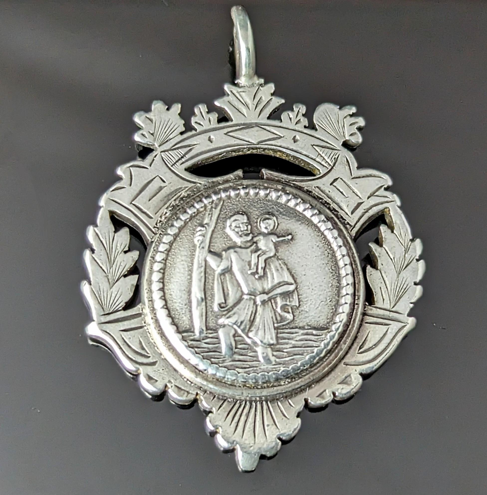 An interesting antique Victorian sterling silver watch fob pendant.

It is a large fob and quite heavy too, it depicts the famous St Christopher image of the saint carrying a child across the mighty river, the patron saint of all travellers.

This