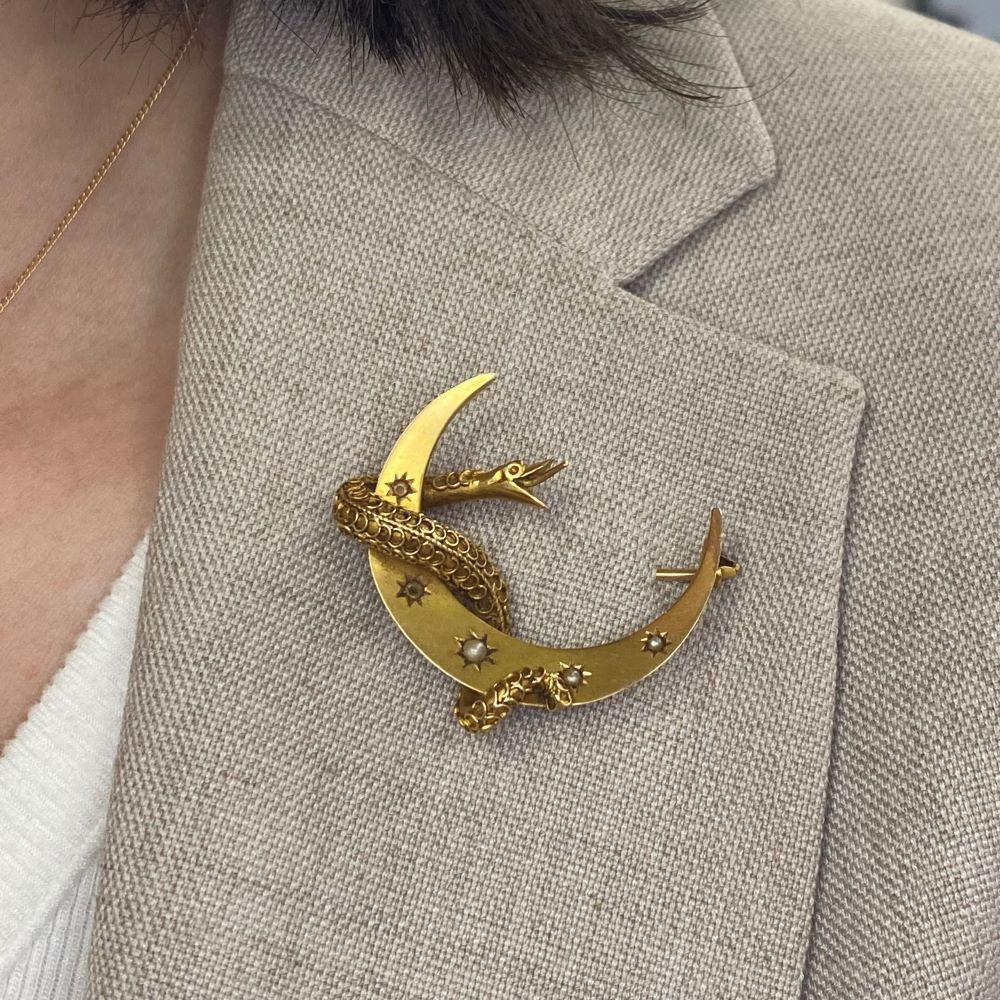 This exquisite antique Victorian brooch, crafted in the 1880s, showcases a mesmerizing design featuring a serpent elegantly coiled around a crescent moon. A symbol of eternity, transformation, and renewal, the snake motif was highly favored during