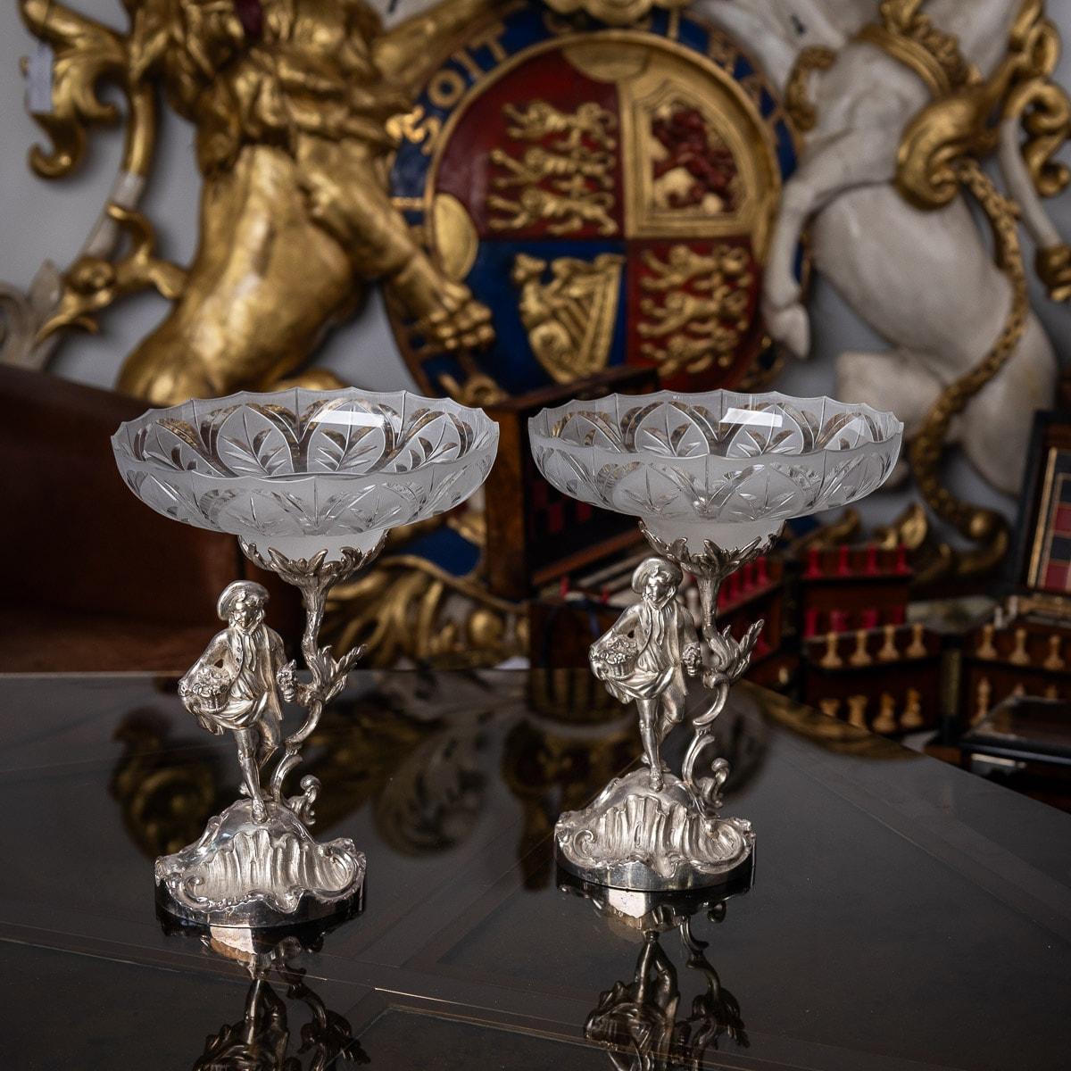 Antica coppia molto rara del 19° secolo di composizioni di novità vittoriane in argento massiccio e vetro tagliato, formate da una coppia di giardinieri maschi in costume del 18° secolo, in piedi su un'elaborata base rococò ed entrambi con in mano